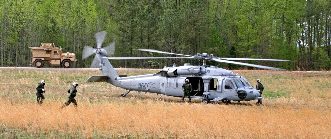 A Navy MH-60S Knighthawk with Helicopter Sea Combat Squadron 26, prepares to pick up Marines of Company B, 1st Bn., 8th Marines, for a training exercise in the landing zone outside Forward Operating Base Phoenix aboard National Guard Maneuver Training Center, Fort Pickett, Va., April 9, 2010. A Navy Mine Resistant Ambush Protection Vehicle drives past the landing zone on its way to refuel.