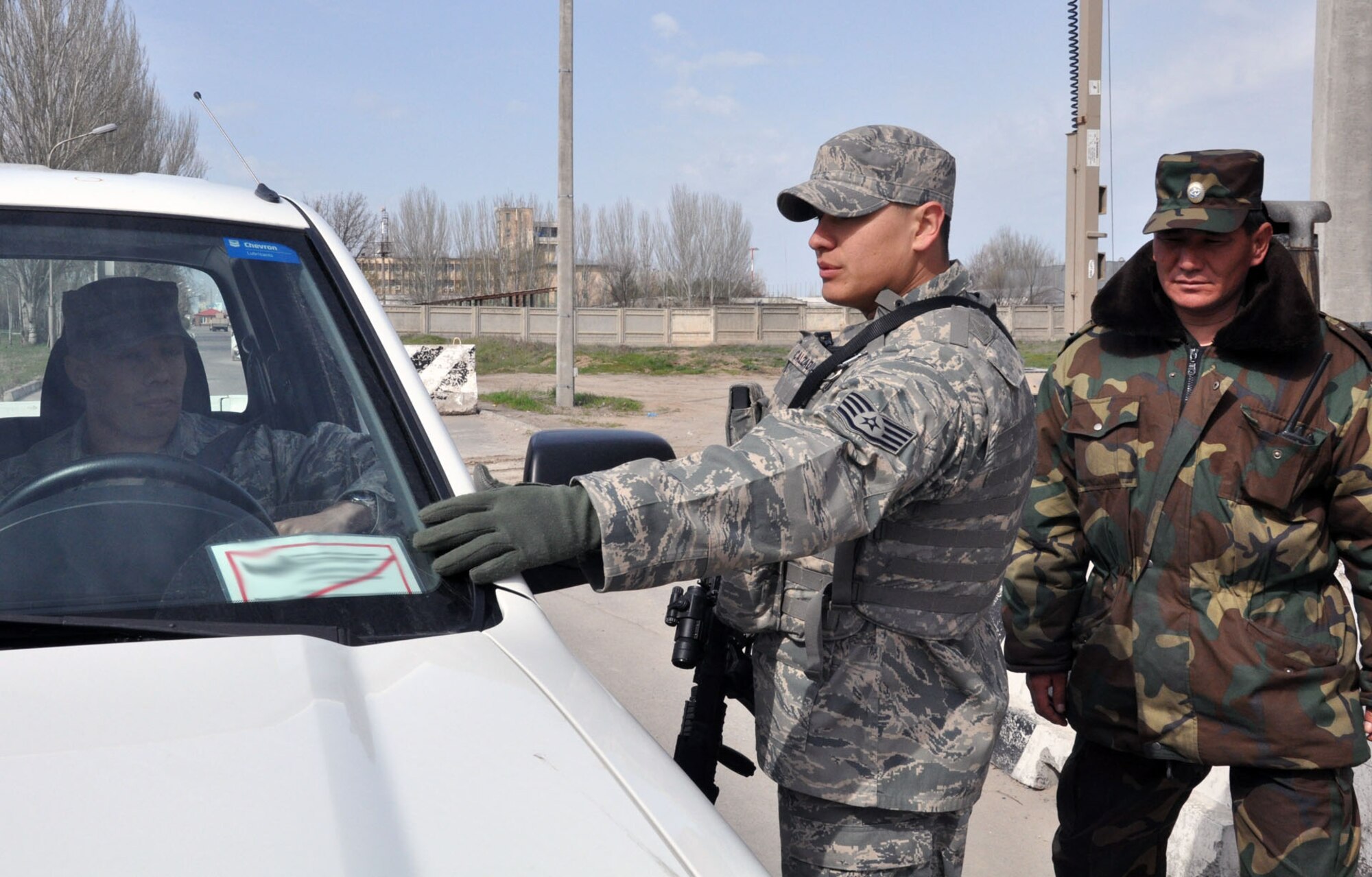 U.S. Air Force Staff Sgt. Francisco Calzadillas and a Manas International Airport security member check the identification cards on a U.S. Air Force government vehicle at an entry control point between the airport and the Transit Center at Manas, Kyrgyzstan, April 10, 2010. Because of the unique mission of the Transit Center at Manas and the strategic U.S. presence in Kyrgyzstan, MIA personnel and 376th Expeditionary Security Forces Squadron members work closely together to ensure the safety and security of the Transit Center, the airport, and all of the members assigned to and working at both installations. (U.S. Air Force photo/Staff Sgt. Carolyn Viss/released)