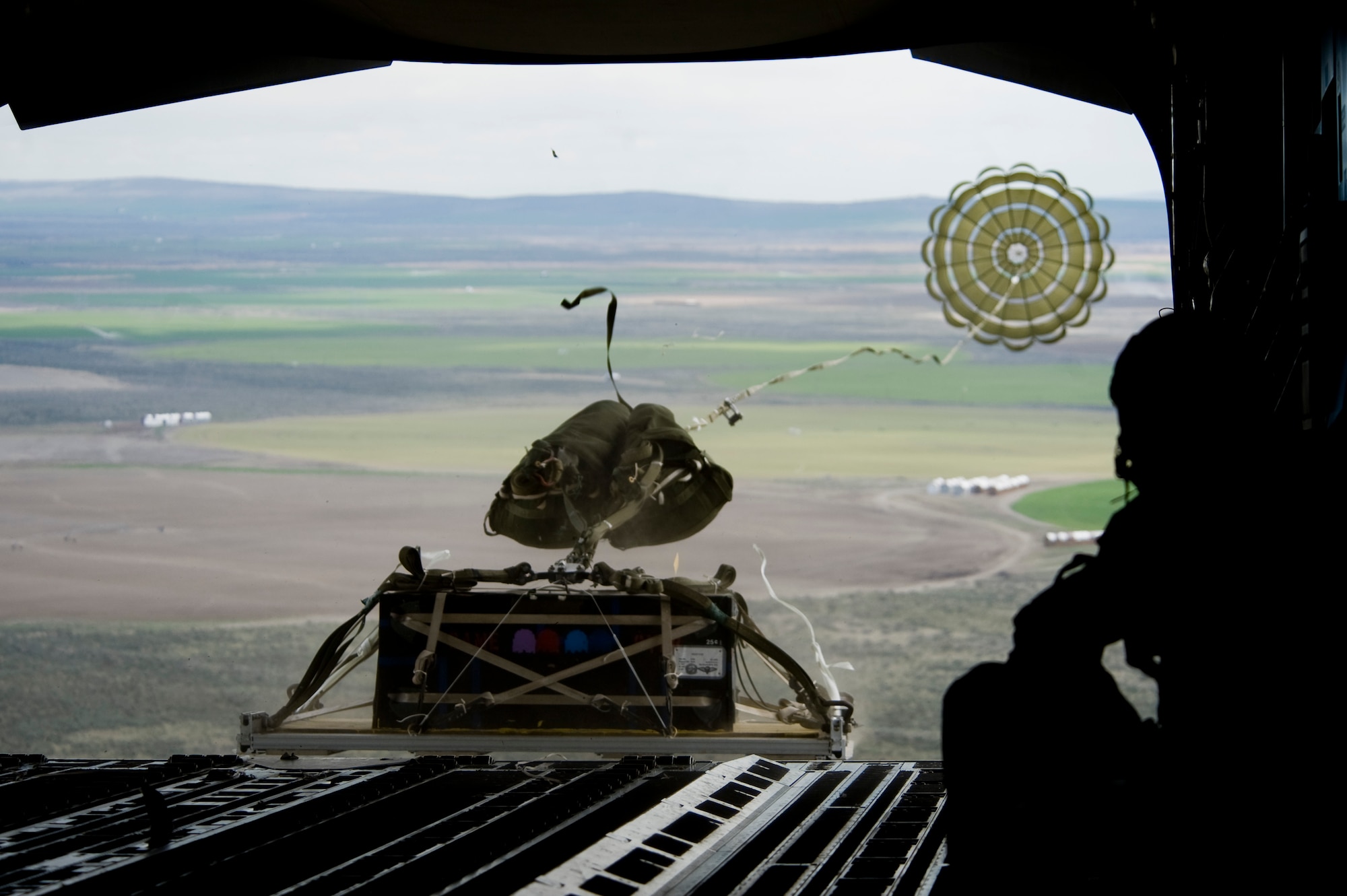 Staff Sgt. Joseph Cimino, 8th Airlift Squadron loadmaster, right, looks on as a heavy airdrop platform extracts from the rear of a C-17 Globemaster III over Moses Lake April 13.  Members of the 8th AS are preparing for an upcoming deployment to the Middle East. (U.S. Air Force Photo by Abner Guzman)