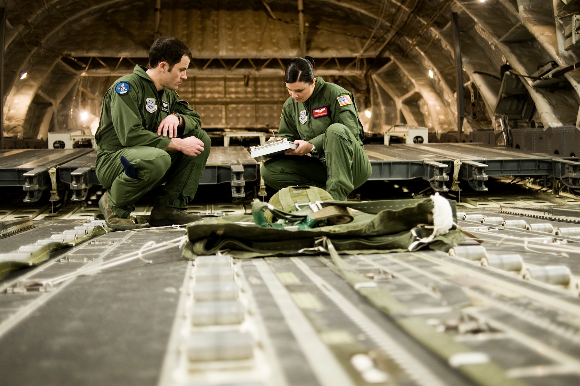 Staff Sgt. Joseph Cimino, 8th Airlift Squadron loadmaster, left, looks on as Staff Sgt. Gigi Gariglio, 62nd Operational Support Squadron, completes a joint airdrop cargo inspection onboard a C-17 Globemaster III April 13.  More than 100 Airmen will deploy with the 8th AS this month.  (U.S. Air Force Photo by Abner Guzman)