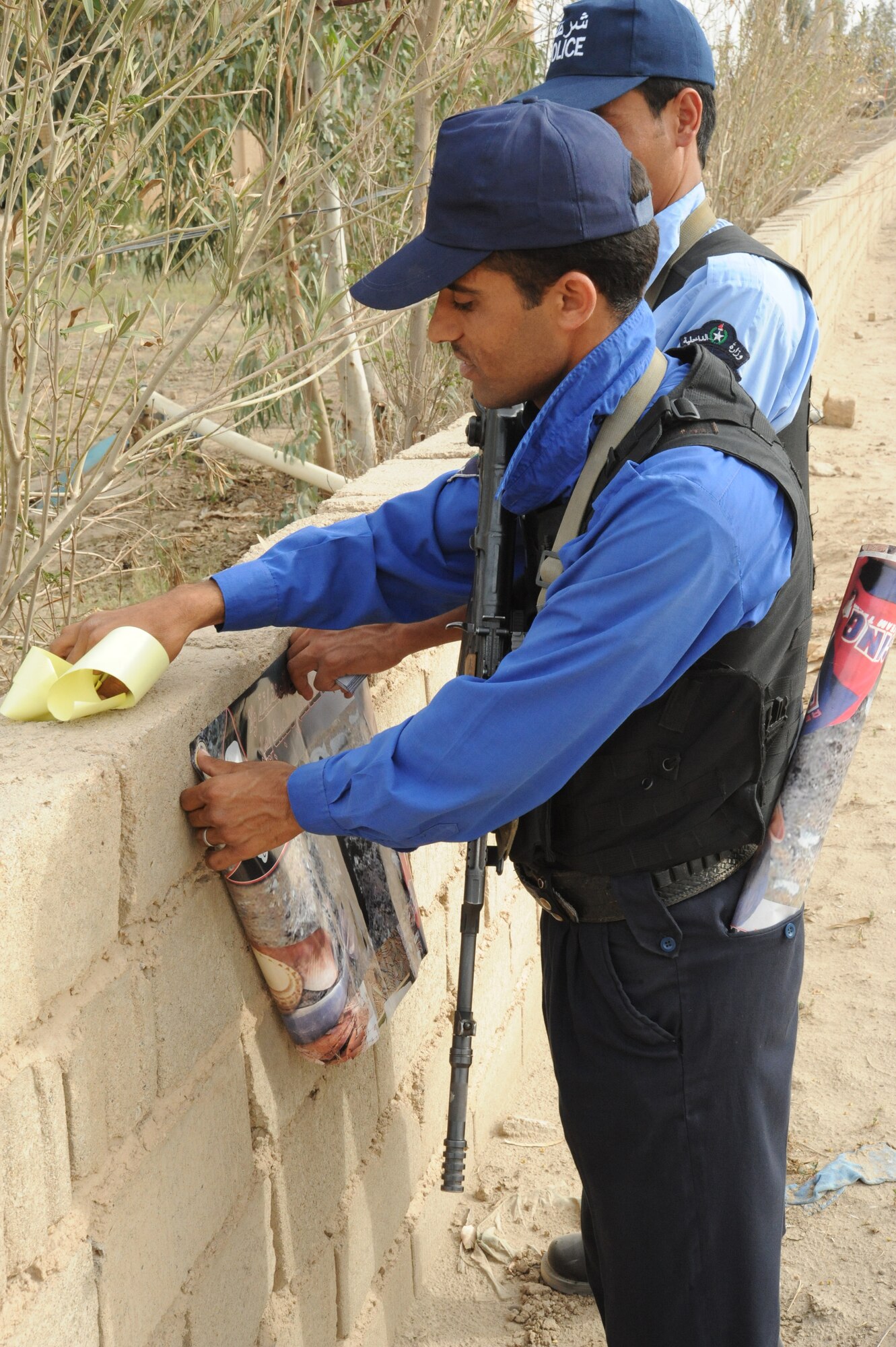 Two members of a local Iraqi Police department place posters on a community wall during a joint presence patrol near Rufush, Iraq, April 4, 2010. The 732nd Expeditionary Security Forces, Detachment 2, conducted a “training and mentoring” mission, which was requested by the local police. During this mission, Air Force personnel trained the police in community policing and assisted with patrolling through a village recently overwhelmed by terrorist attacks.  (U.S. Air Force photo/Master Sgt. Trish Bunting/ Released)
