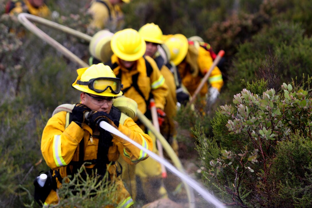 Ray C. Valdez, a firefighter with Camp Pendleton’s Fire and Emergency Services and former Marine, simulates extinguishing a fire during the department’s first Multi-company Hoselay and Rule of Engagement Drill at Camp Pendleton, April 14. More than 130 firefighters from the base’s 11 fire stations participated in the special exercise, April 14 - 16. The drill took firefighters through simulated wildfire scenarios that forced them to negotiate steep and virtually inaccessible terrain, in preparation for the fast approaching fire season.