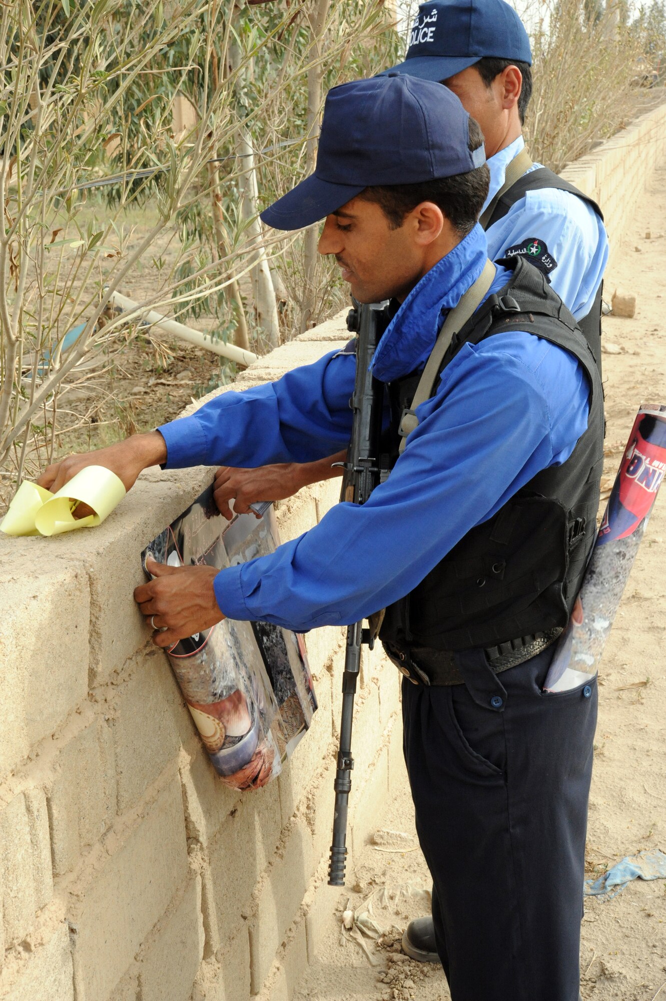 Two members of an Iraqi police department place posters on a community wall during a joint presence patrol April 4, 2010, near Rufush, Iraq. (U.S. Air Force photo/Master Sgt. Trish Bunting)
