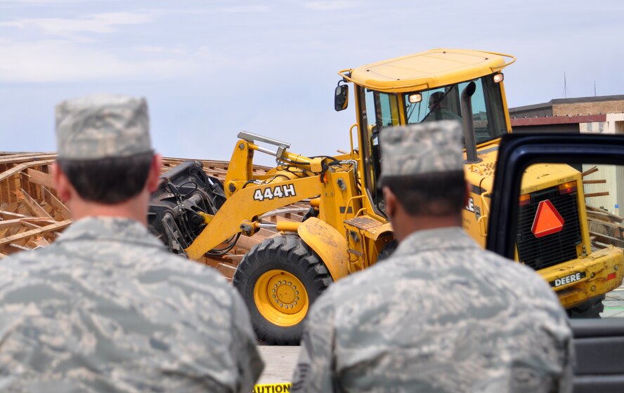 Safety observers from the 419th Civil Engineering Squadron stand by as Staff Sgt. Paul Schatzman, also of CES, uses a front end loader to bring down Bldg. 29. The building, located near the aircraft ramp, was demolished April 10 to make room for a new facility that will house personnel from the 466th Fighter Squadron Aircraft Maintenance Unit. (U.S. Air Force photo/Staff Sgt. Alan Schultz)