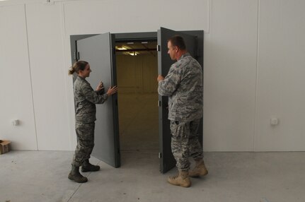 Second Lt. Danielle Dowds (left) and Capt. Steve Soliday, both from the 902nd Logistics Readiness Squadron, open the doors of the new vault storage area that will house weapons and ammunition for Airmen who process the deployment line prior to a deployment. (U.S. Air Force photo by Rich McFadden)