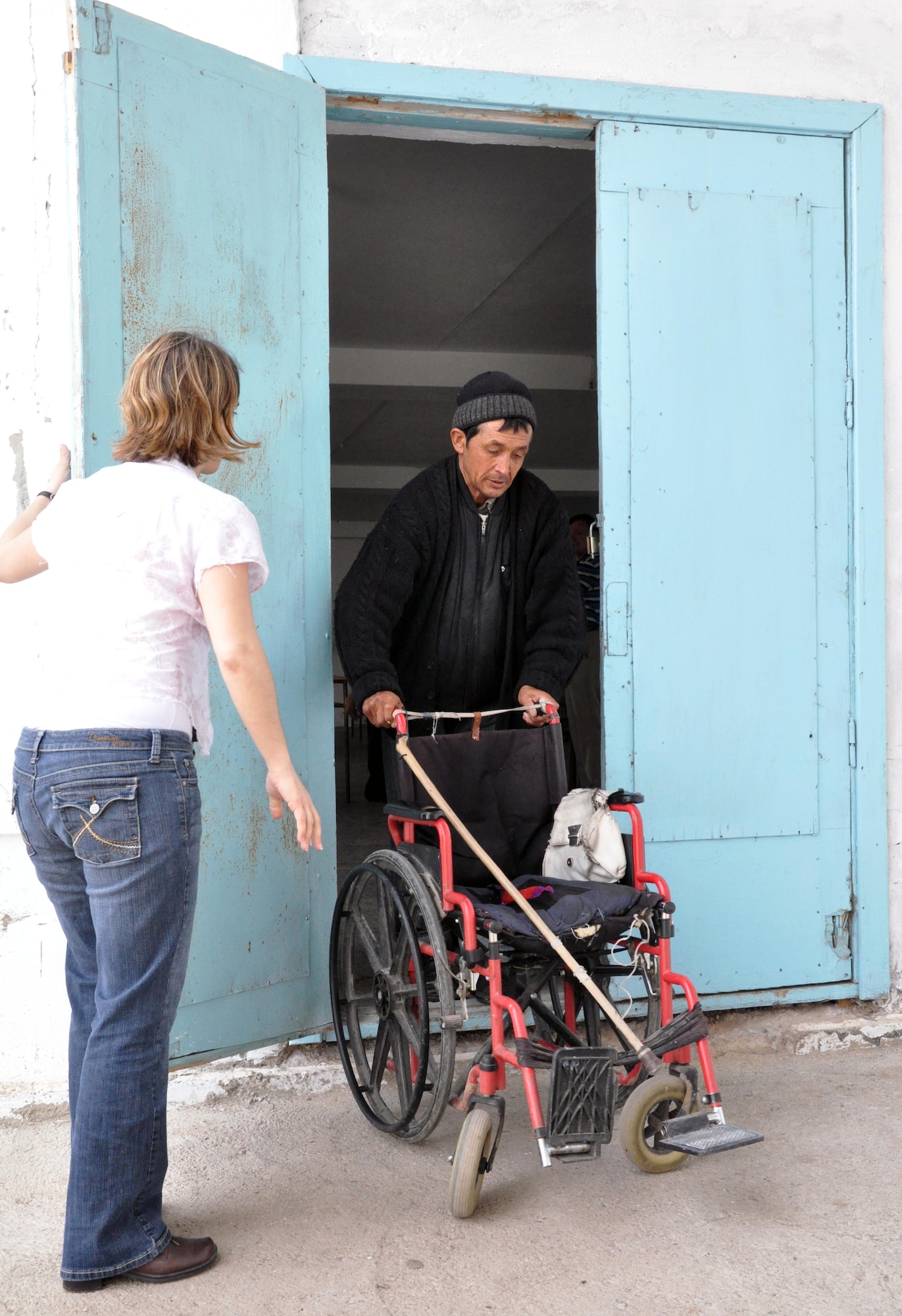U.S. Air Force Tech. Sgt. Jamie McCarrison helps a resident of the TokMok Psychoneurologic Boarding House make it out the door with his wheelchair during a humanitarian assistance visit April 14, 2010, in Iskra Village, Kyrgyzstan. This boarding house hosts 255 male patients and is badly in need of repair and basic amenities. Airmen from the Transit Center at Manas visited to bring food, clothing, and some entertainment items and to see how they can help the boarding house in the future. (U.S. Air Force photo/Staff Sgt. Carolyn Viss)