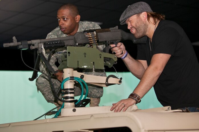 NEVADA TEST AND TRAINING RANGE --  Staff Sgt. Bruce Thompson Jr. of the 99th Ground Combat Training Squadron assists country music singer James Otto to fire an M240B machine gun from atop a HUMVEE in the 99th GCTS virtual simulator April 17, 2010. The Academy of Country Music and the USO  toured  the 99th GCTS before performing a free concert for Nellis Air Force Base.  (U.S. Air Force photo by Tech. Sgt. Michael R. Holzworth)

