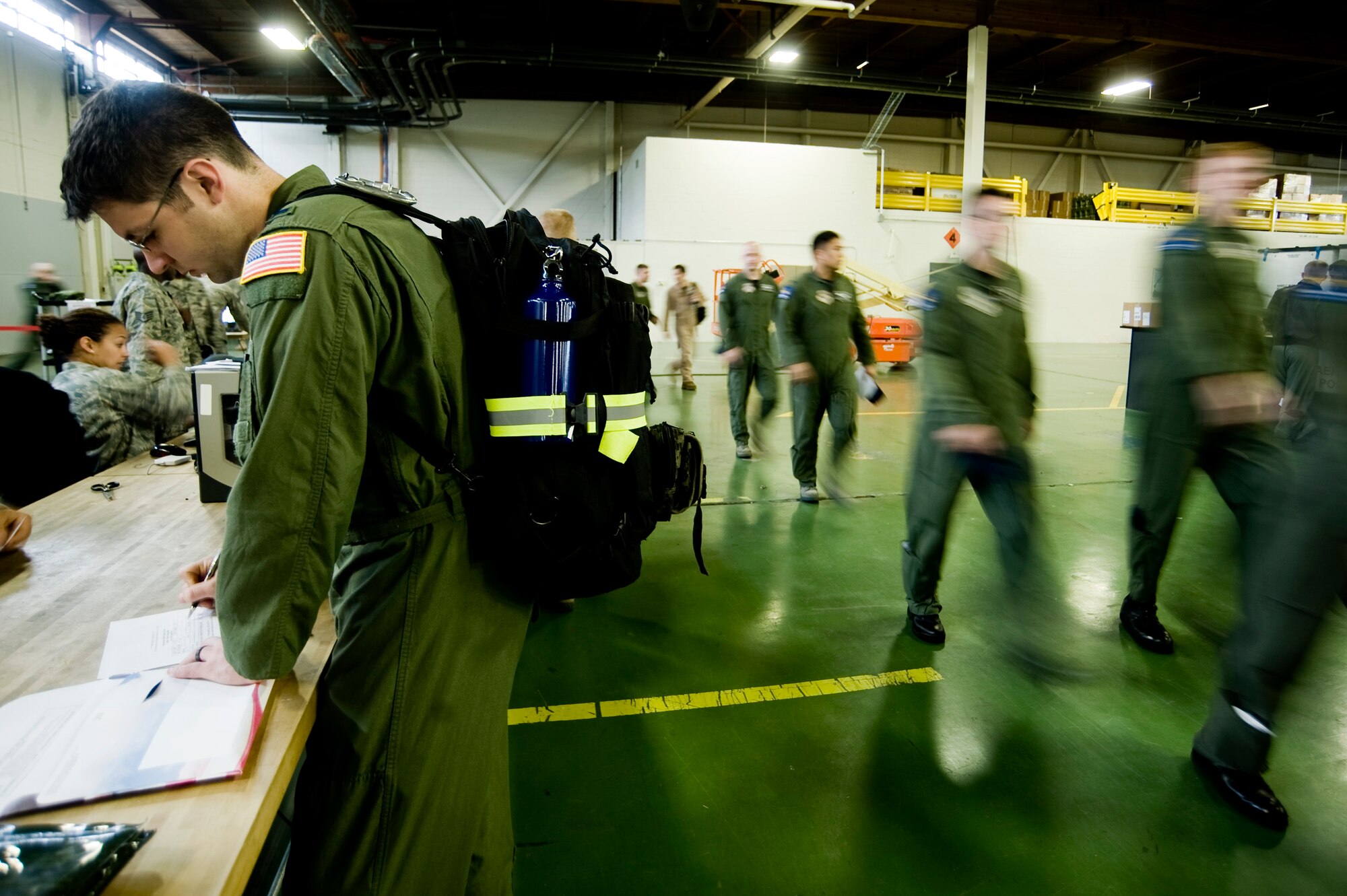 1st Lt. Robert Campbell, 8th Airlift Squadron, left, checks out a gas mask canister at the Logistics Readiness Squadron mobility warehouse April 20 as additional members of the squadron arrive for processing in preparation for an upcoming deployment.  More than 100 members of the 8th AS are deploying for approximately 120 days to the Middle East. (U.S. Air Force Photo by Abner Guzman)