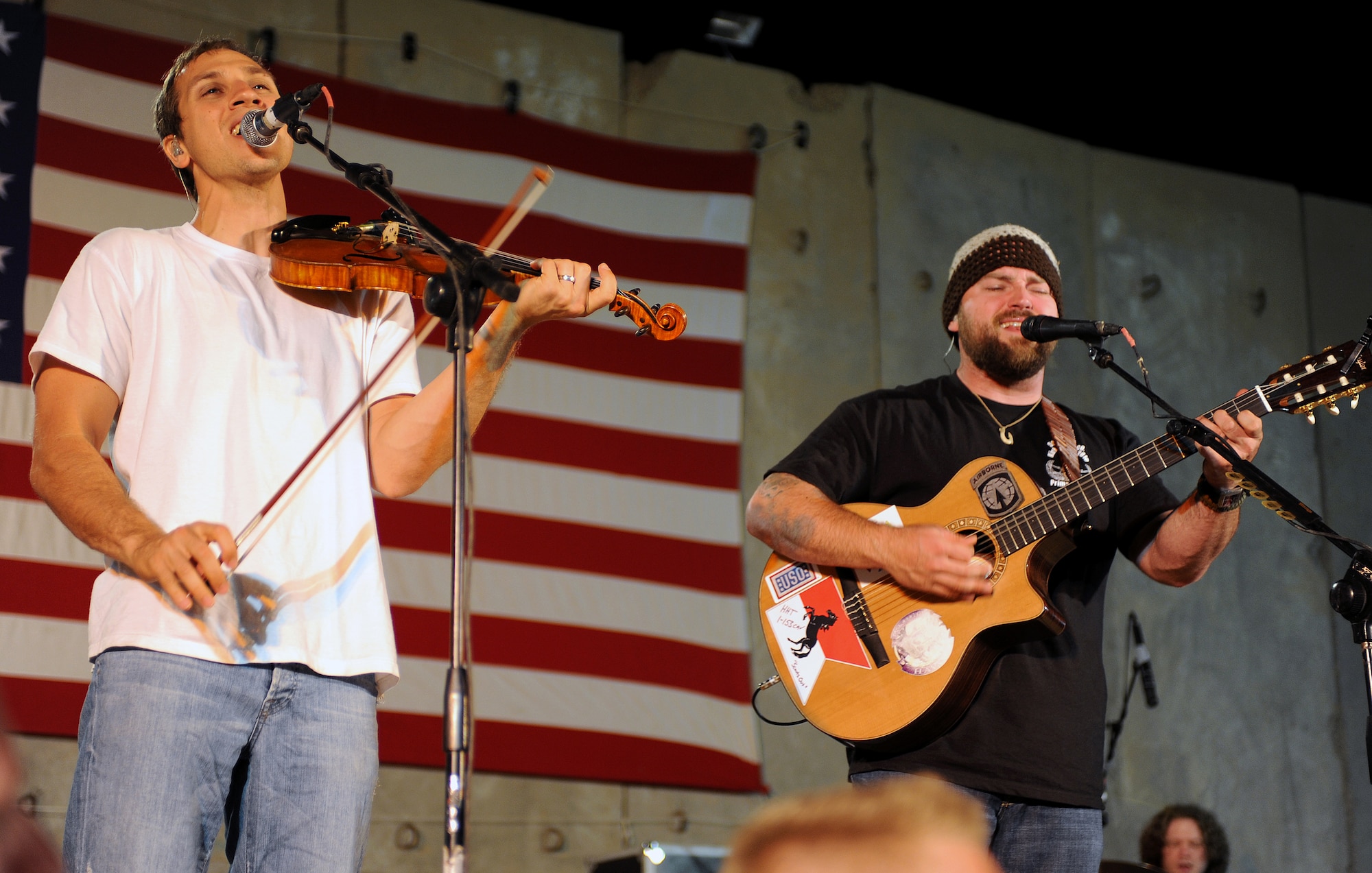 Zac Brown (right) and Jimmy De Martini, members of the Zac Brown band perform for a crowd of deployed personnel at Holt Stadium at Joint Base Balad, Iraq, April 18, 2010. The Grammy-nominated band is touring various bases throughout Southwest Asia to perform for the troops rather than attend this year's Academy of Country Music Awards for which they were nominated for several awards. (U.S. Air Force photo by Master Sgt. Linda C. Miller/Released)