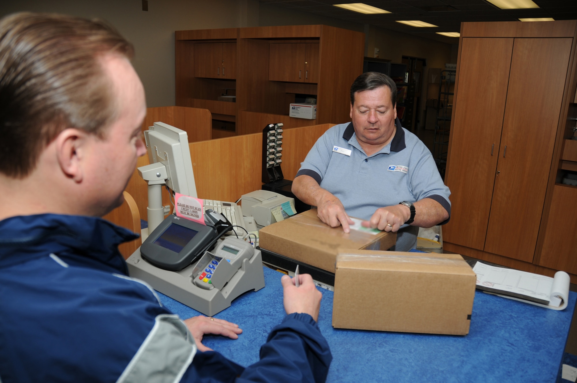 Master Sgt. Matthew Calvert, 334th Training Squadron, gives post office lead clerk Gary Kostmayer packages to mail at the new post office Monday.  The new facility consolidates Keesler’s post office with the base informtion transfer system official mail center and the current postal service center for permanent-party personnel.  (U.S. Air Force photo by Kemberly Groue)