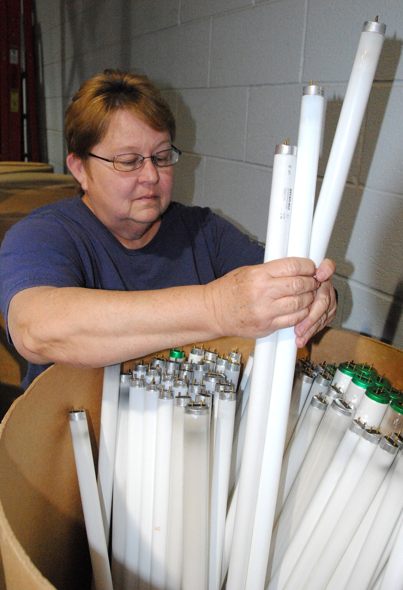 Carol Earhart, a material acquisition specialist with CSC Applied Technologies Civil Engineering at Vance, loads spent fluorescent bulbs into a shipping barrel. The barrel, which can hold more than 150 bulbs, will be sent to a recycler in Texas. (U.S. Air Force photo/ Joe B. Wiles)