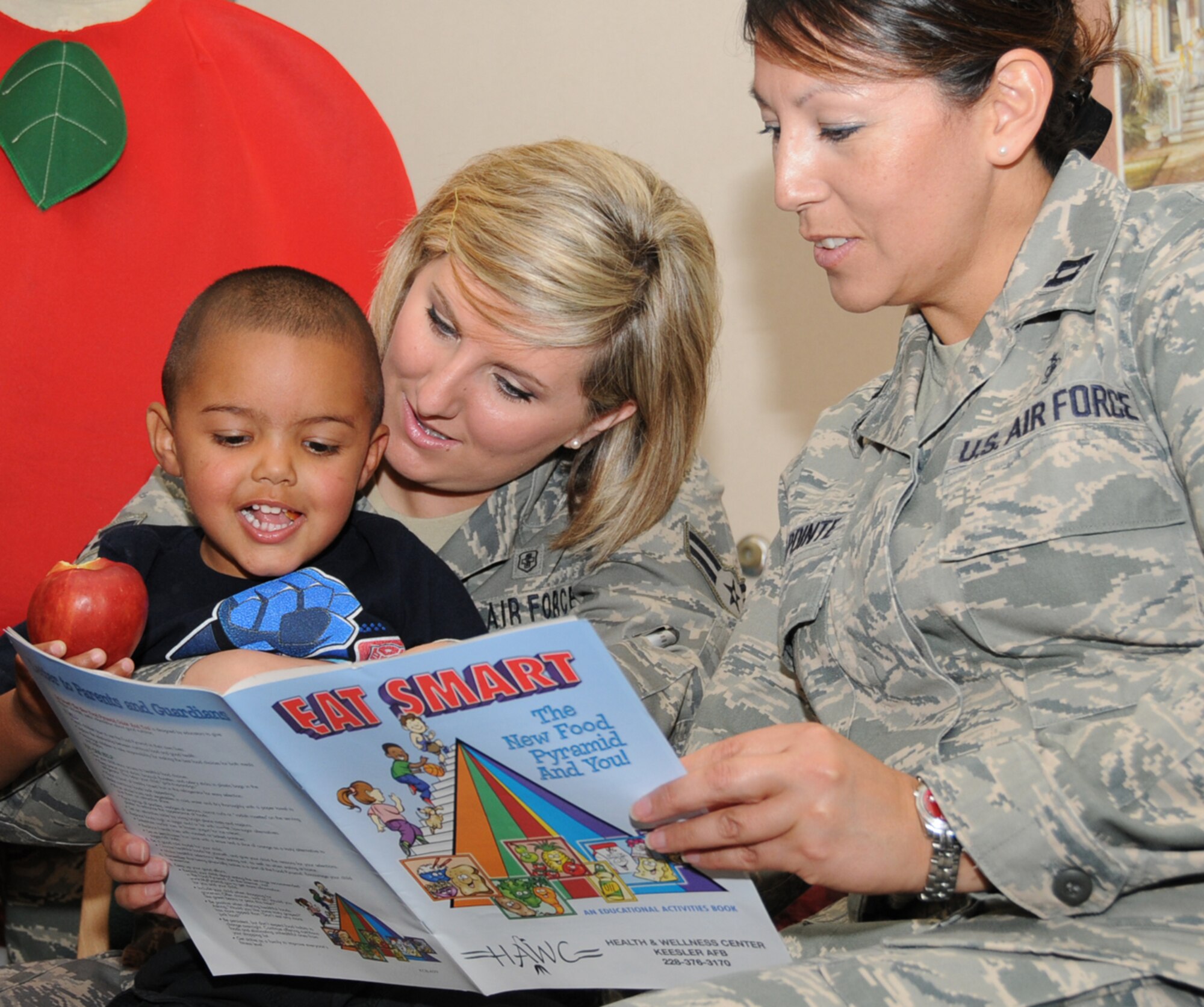Two-year-old Christian Threatt munches an apple while he’s held by his mom, Airman 1st Class Melissa Burrows as Capt. Donna LaPointe reads a booklet on healthy eating from the health and wellness center during a nutrition presentation April 16 at McBride Library.  Airman Burrows and Captain LaPointe are from the 81st Medical Operations Squadron.  (U.S. Air Force photo by Kemberly Groue)