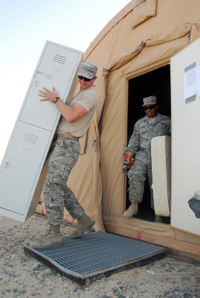 U.S. Air Force Airman 1st Class Dustin Kimbrough and Tech. Sgt. Willie Andino, both of the 386th Expeditionary Force Support Squadron Commando Village lodging staff, move furniture from a storage tent April 19, 2010 at an air base in Southwest Asia. (U.S. Air Force photo by Tech. Sgt. Lindsey Maurice/Released)