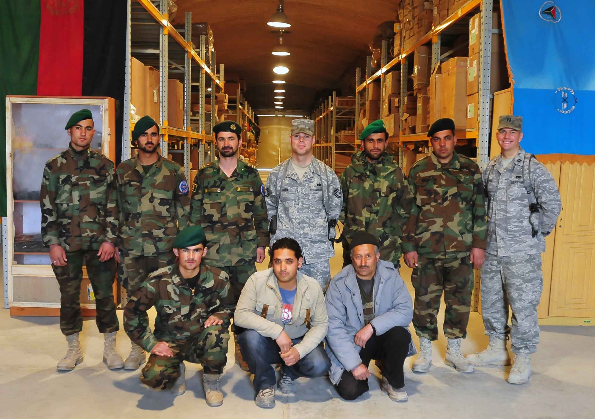 Members of the Afghan National Army Air Corps and their mentors , Airmen from the 439th Air Expeditionary Advisory Squadron, Mission Support Group, of the 438th Air Expeditionary Wing, Combined Air Power Transition Force, pause for a photo at the general purpose warehouse in Kabul, Afghanistan. (U.S. Navy photo/MC2 David Quillen)