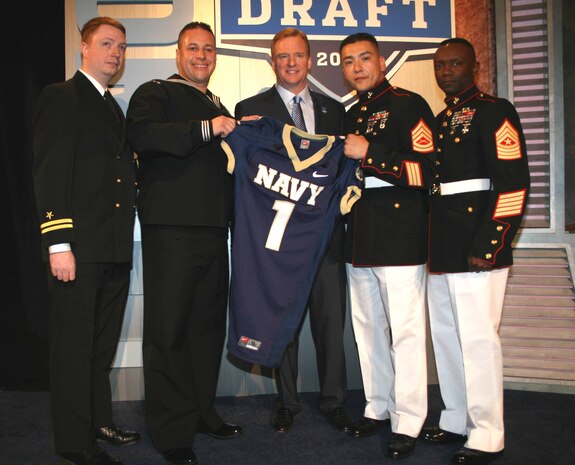 Gunnery Sgt. Willie C. Cisneros III, Assistant Marine Officer Instructor, NROTC Unit SUNY Maritime College, Fordham University and Molloy College, and Sgt. Maj. Samuel Heyward Jr, Recruiting Station New York sergeant major, hold a United States Naval Academy football jersey presented to Roger S. Goodell, National Football League commissioner, April 26, New York.