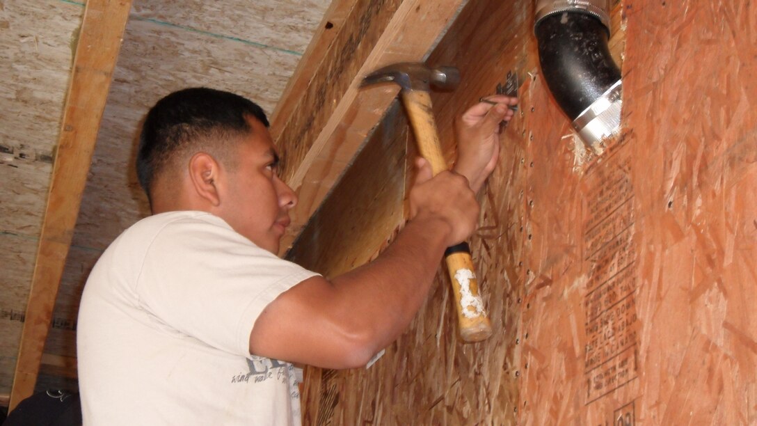 Cpl. Alberto Vazquez, water support technician, support company, utility platoon, 7th Engineer Support Battalion, 1st Marine Logistics hammers in a few nails to help build the support beams of a house, April 22.
