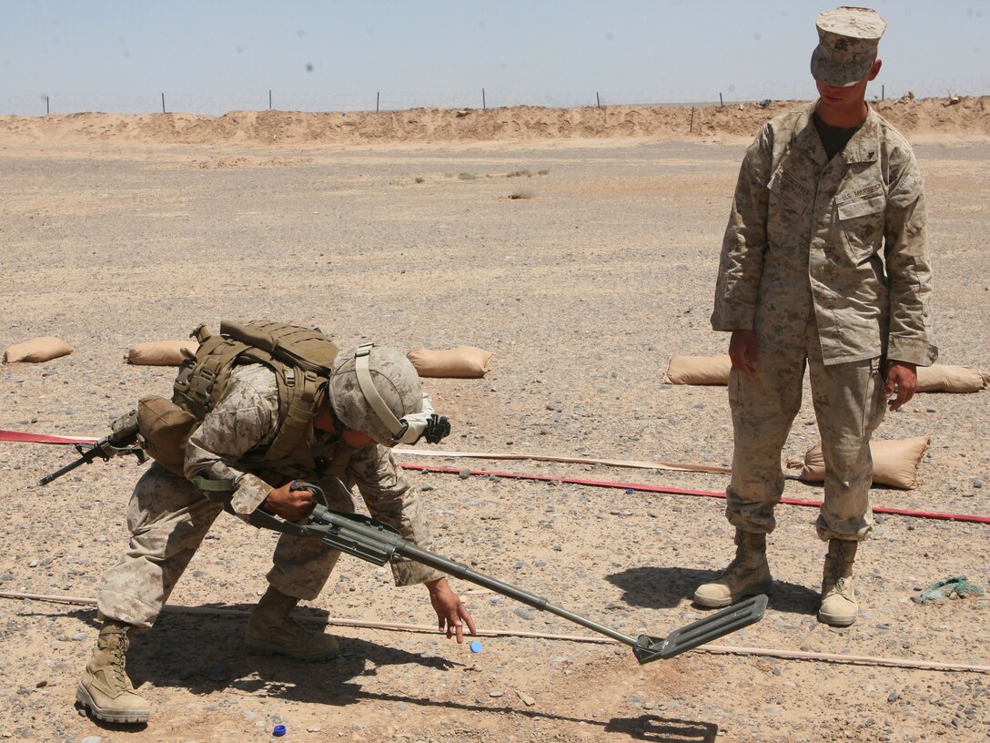Lance Cpl. Vernon K. Akina, a food service specialist with 3rd Battalion, 1st Marine Regiment, marks a notional improvised explosive device while Lance Cpl. Nicholas A. Weissgerber, a compact metal detector instructor with 3rd Combat Engineer Battalion, watches during IED lane training at Camp Dwyer, Helmand province, Afghanistan, April 24. Akina located the notional IED with a compact metal detector during the practical application portion of reception staging, onward movement and integration training and integration training.
