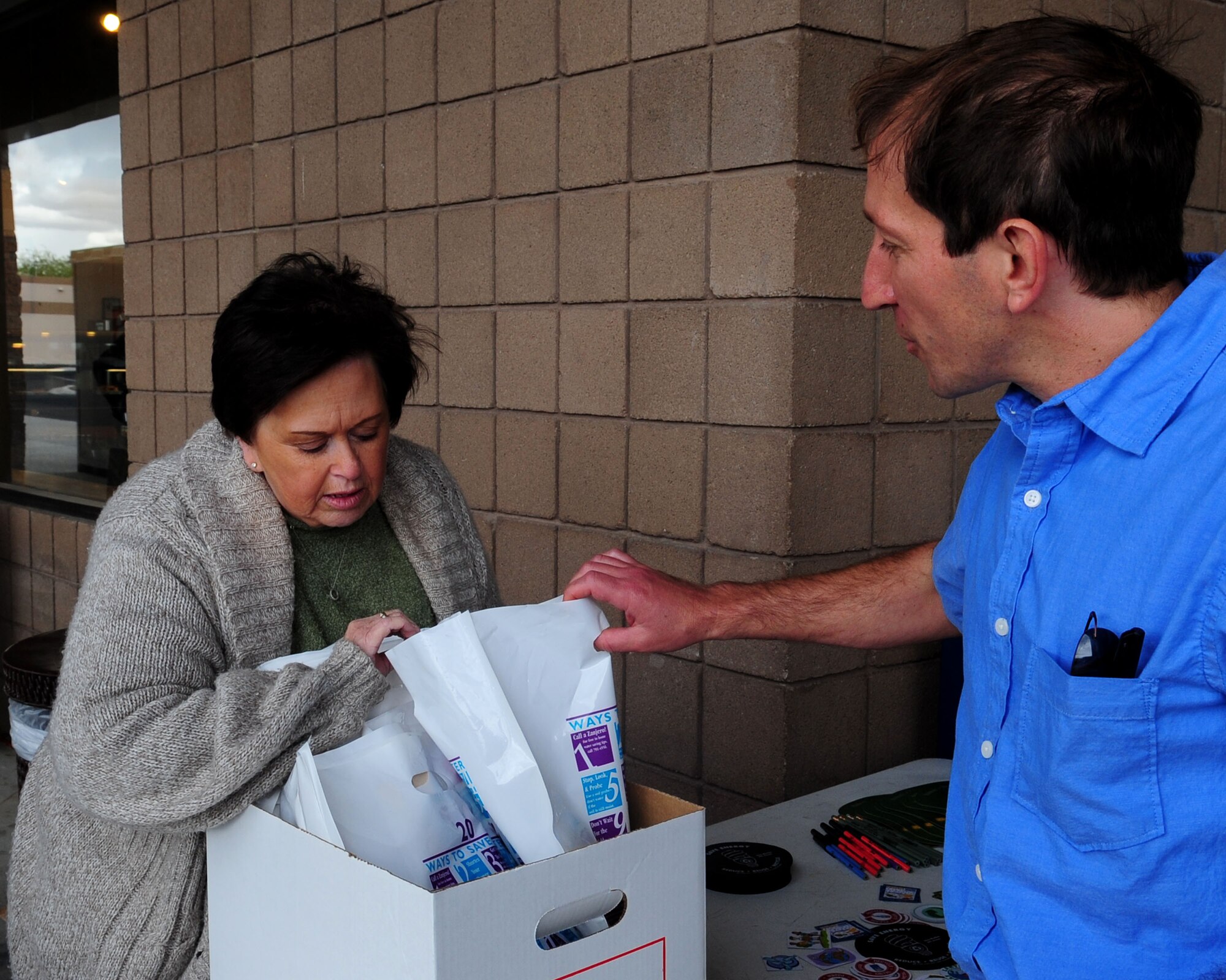 Gwen Lisa, 355th Civil Engineer Squadron Natural/Cultural Resource manager, hands a gift bag to Jake Mennella an architect from the 355th CES, in celebration of Earth Day at the Base Exchange here April 22. Airmen and families from Davis-Monthan joined the global community in promoting environmental protection and appreciation today by observing the 40th annual Earth Day. The 355th CES helped bolster the effort with a display at the Base Exchange, where they handed out informational packets and offered story boards with the base’s energy conservation efforts. (U.S. Air Force photo/Airman Jerilyn Quintanilla)