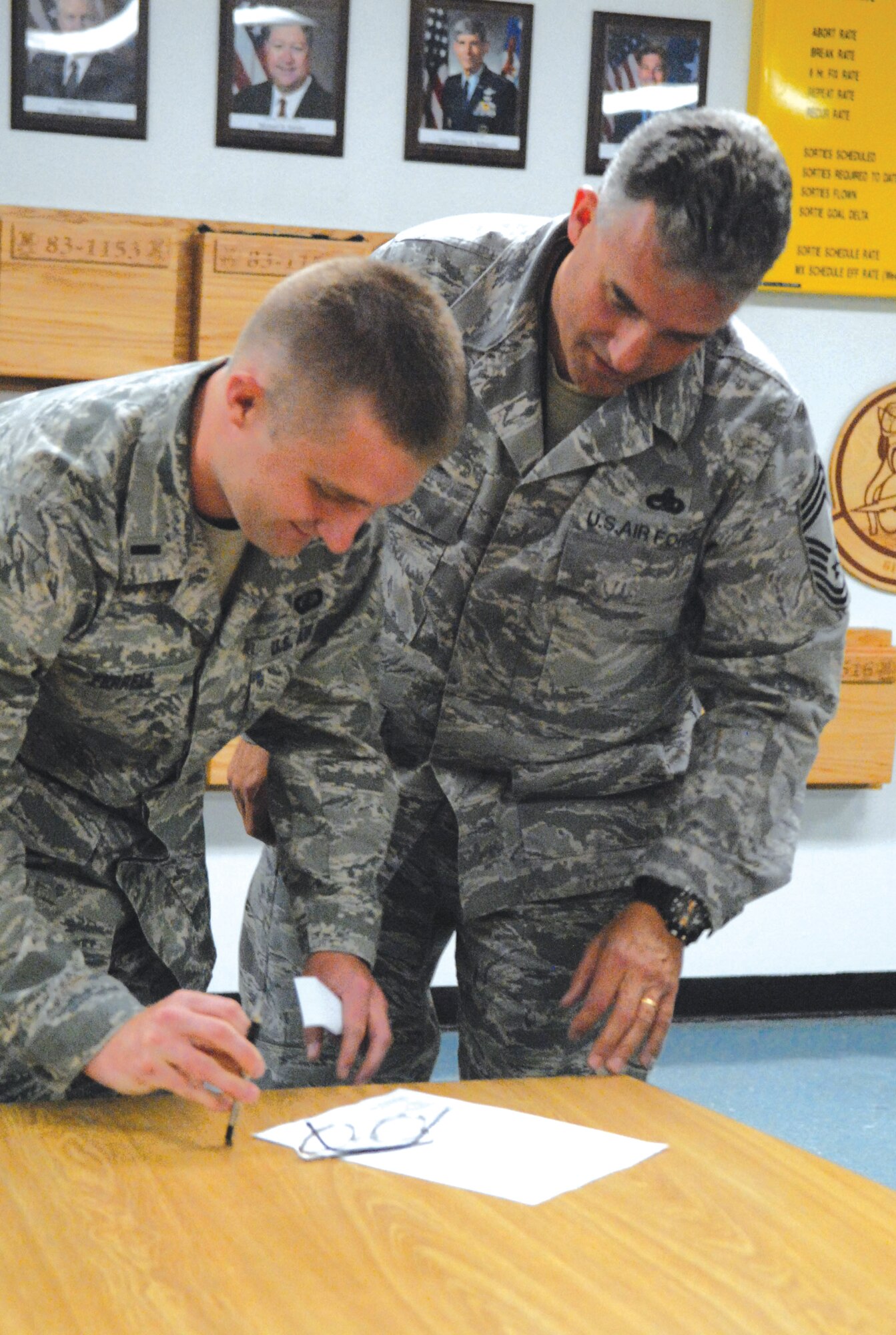 First Lt. Steve Ferrell, 28th Test and Evaluations Squadron operations analyst at Eglin Air Force Base, Fla., signs enlistment paperwork April 9 for his father, Chief Master Sgt. Steven Ferrell, 61st Aircraft Maintenance Unit superintendant. Lieutenant Ferrell flew in to Luke to swear-in his father and did it in front of about 150 Airmen in the 61st AMU. (photo by 2nd Lt. Ryan DeCamp) 