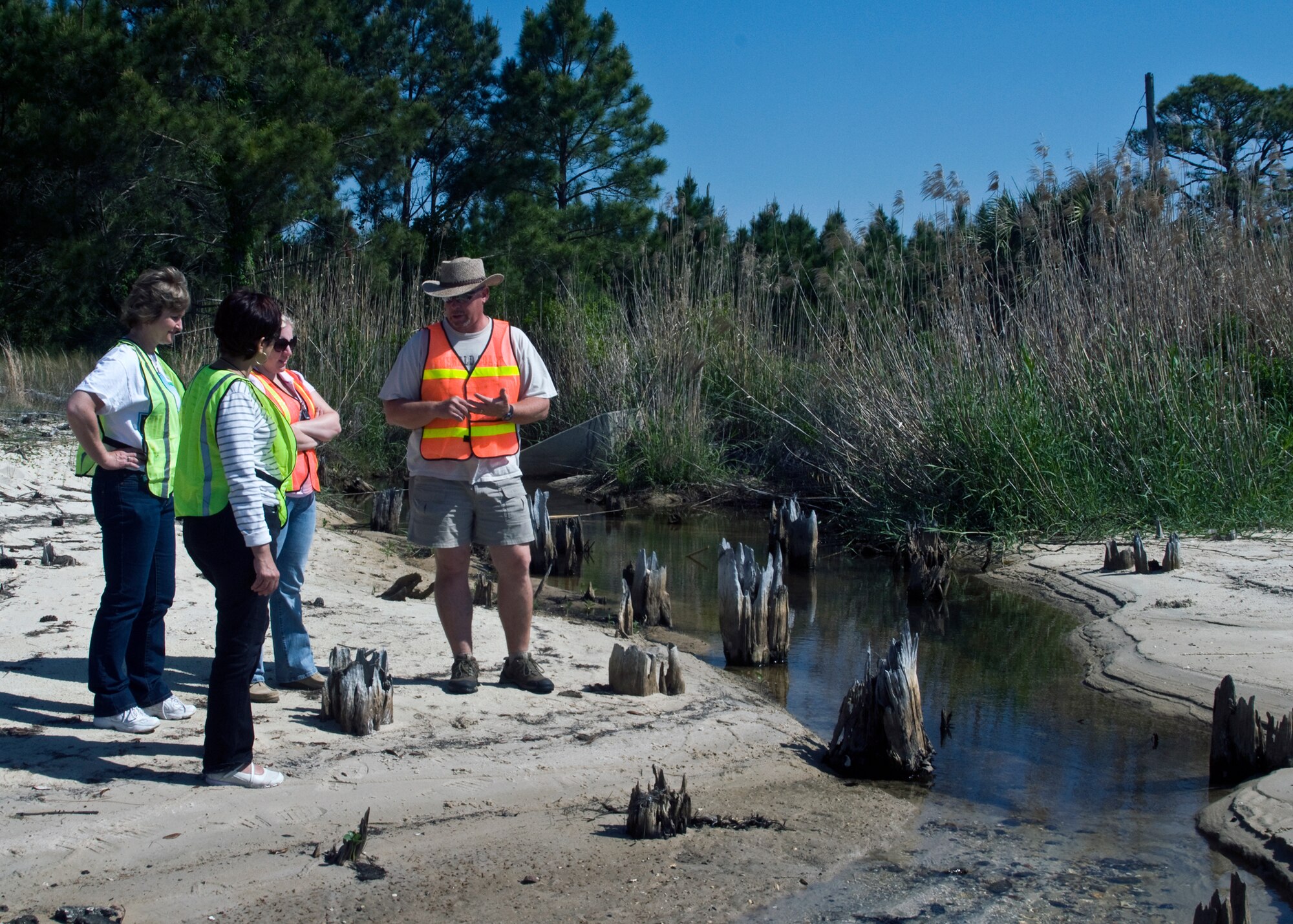 Standing at one of Eglin’s stormwater discharge points, Tim Langley, 96th Civil Engineer Group’s  Environmental Compliance Branch, explains to Earth Day volunteers that any contaminates dumped or washed into Eglin’s storm drains by rain  can end up here and enter the Choctawhatchee Bay. Approximately 13 volunteers applied  152 “No Dumping, Drains to Bay” markers on storm drains around the base April 22.  (Air Force photo/Scott Moorman.)
