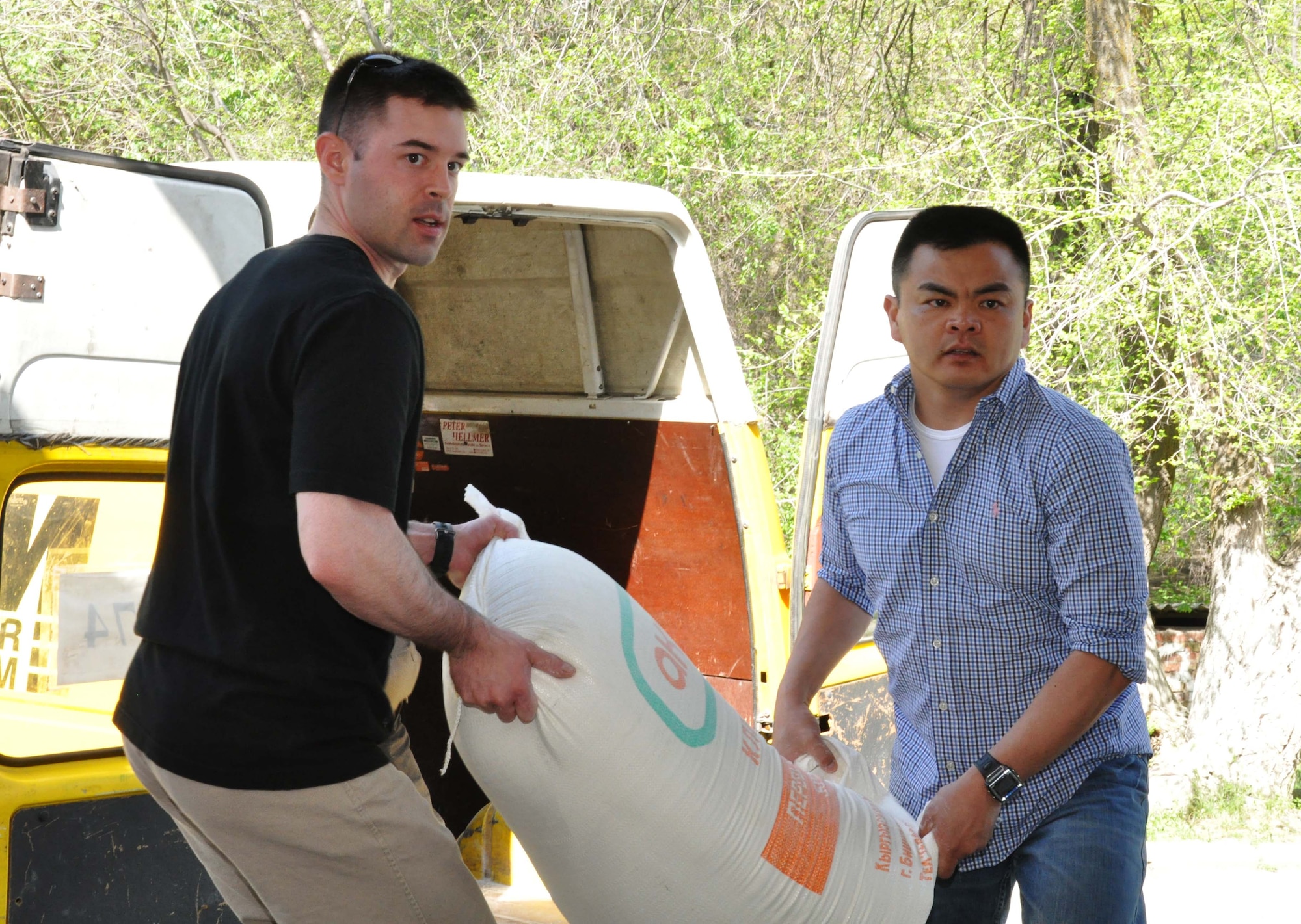Tech. Sgt. Wes Engle and Capt. Tom Mulka, Airmen from the Transit Center at Manas, Kyrgyzstan, carry a 100-pound bag of flour into the Sokulukskaya Special Boarding School/orphanage for children April 23, 2010. Most of the 270 children there have had or need cleft palette surgery. (U.S. Air Force photo/Staff Sgt. Carolyn Viss)