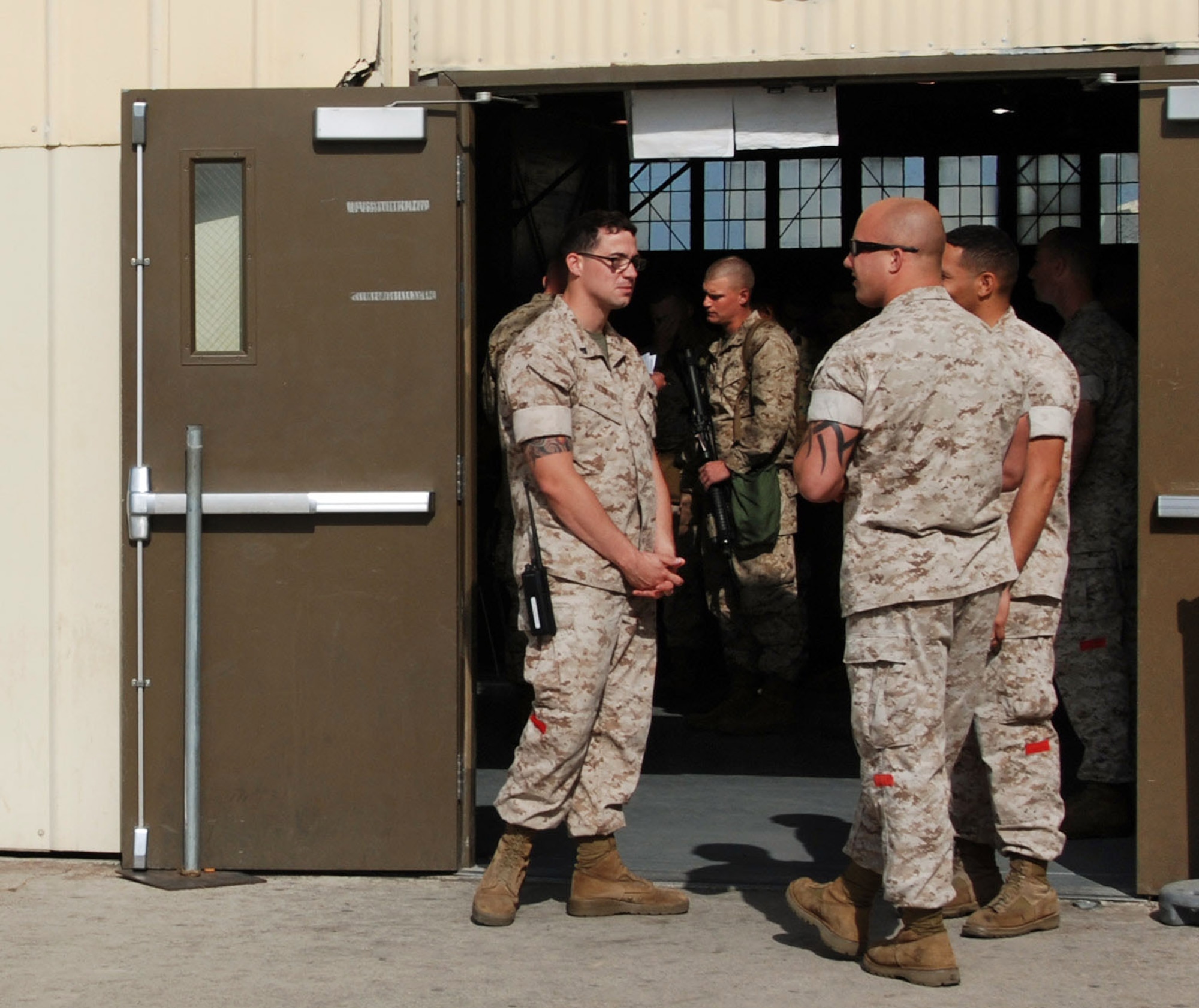 Cpl. Renold Oliver (left) talks to Cpl. Cody Kramer outside the deployment hangar at March ARB. The red patches visible on their trouser legs distinguish the Marines as landing support specialists. (U.S. Air Force photo by Megan Just)