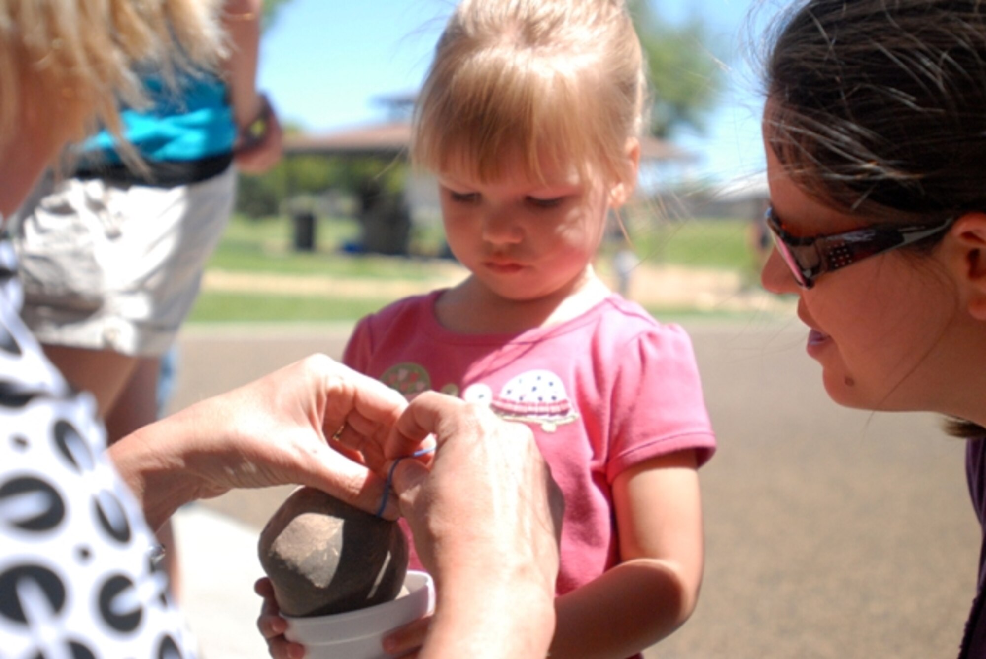 Kaitlyn Tucker, 2, holds on tight as Michelle DeRusso, Concho Valley Master Gardners, puts the finishing touches on her Plant Pal. More than 50 Plant Pals, filled with soil and grass seeds, were made during the Children’s Festival April 24. (U.S. Air Force photo/Connie Hempel)