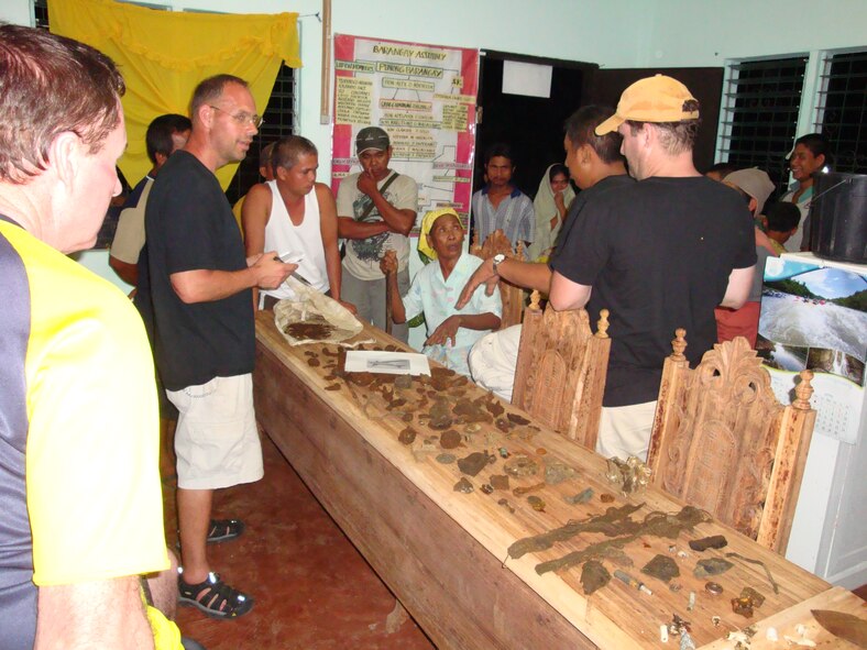 TACLOBAN, Philippines -- An 80-year-old village elder sits at the center of the table looks over pieces of a C-47 Skytrain crash from World War II, from which six servicemembers were listed as “missing in action”. (Photo courtesy of Senior Master Sgt. Thomas Niznik/RELEASED)