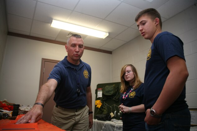 Navy Chief Robert P.K. Craig, a Hospital Corpsman Chief assigned to the Cherry Point Aviation Survival Training Center, shows Skylar E. Kowalski and Jared G. Kopecky, both 8th graders from H.J. MacDonald Middle School of New Bern, samples of surival training gear used by pilots and aircrew who undergo training at ASTC, during an April 27 Student at Work Initiative project. A total of 20 students from H.J. MacDonald Middle School and Grover C. Fields Middle School of New Bern, visited the air station to shadow Marines, Sailors and Department of Defense civilians who maintain individual work-centers throughout the air station.