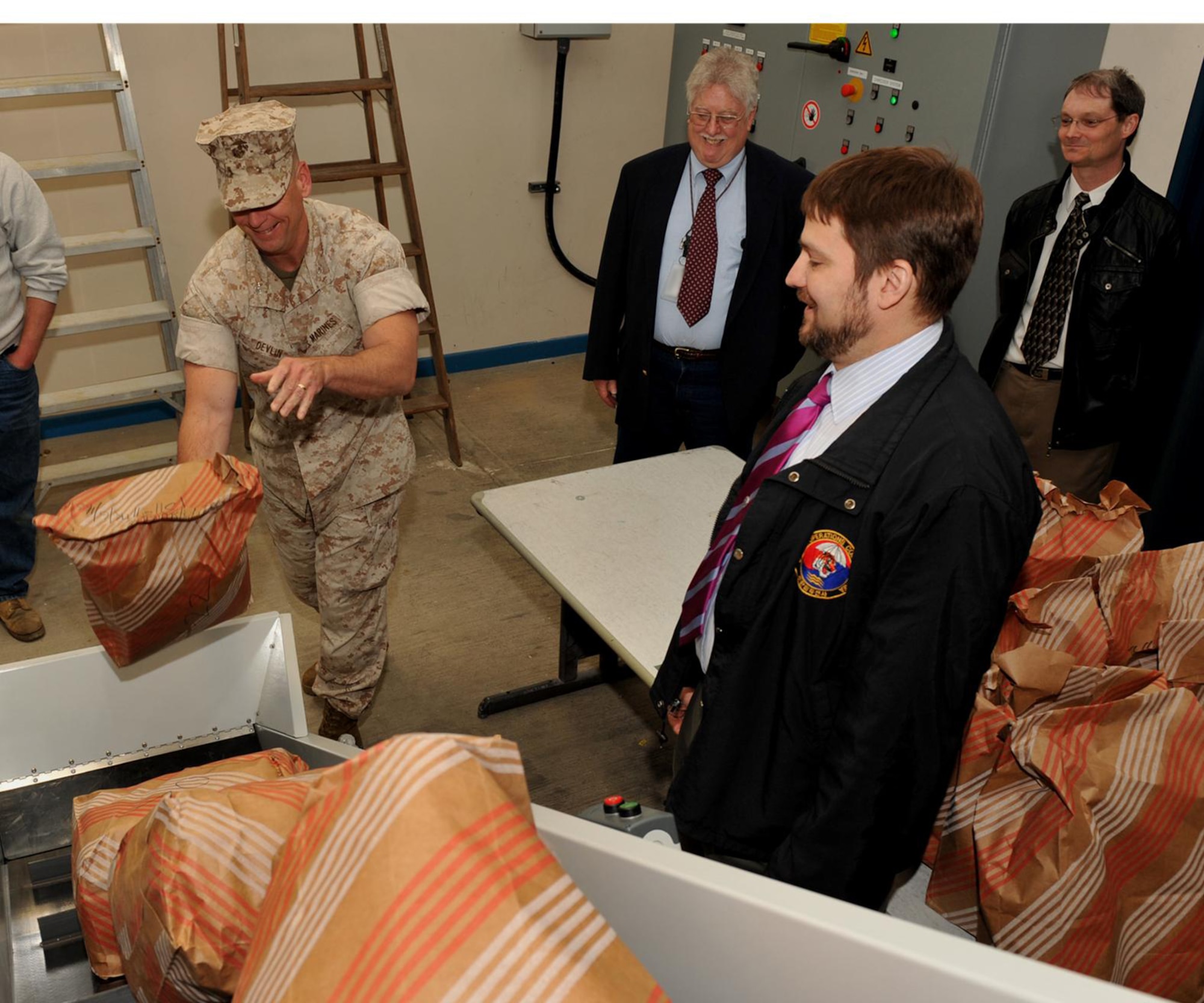 Marine Corps Colonel Pete Devlin, JIOCEUR Analytic Center Commander tosses the first burn bag into the new industrial shredder at RAF Molesworth as JAC Chief of Installation Management, Mr. Robert J. James and JAC Chief of Security Support Mr. Joseph P. Bowen look on.  U.S. Air Force Photo by Staff Sgt. Javier Cruz