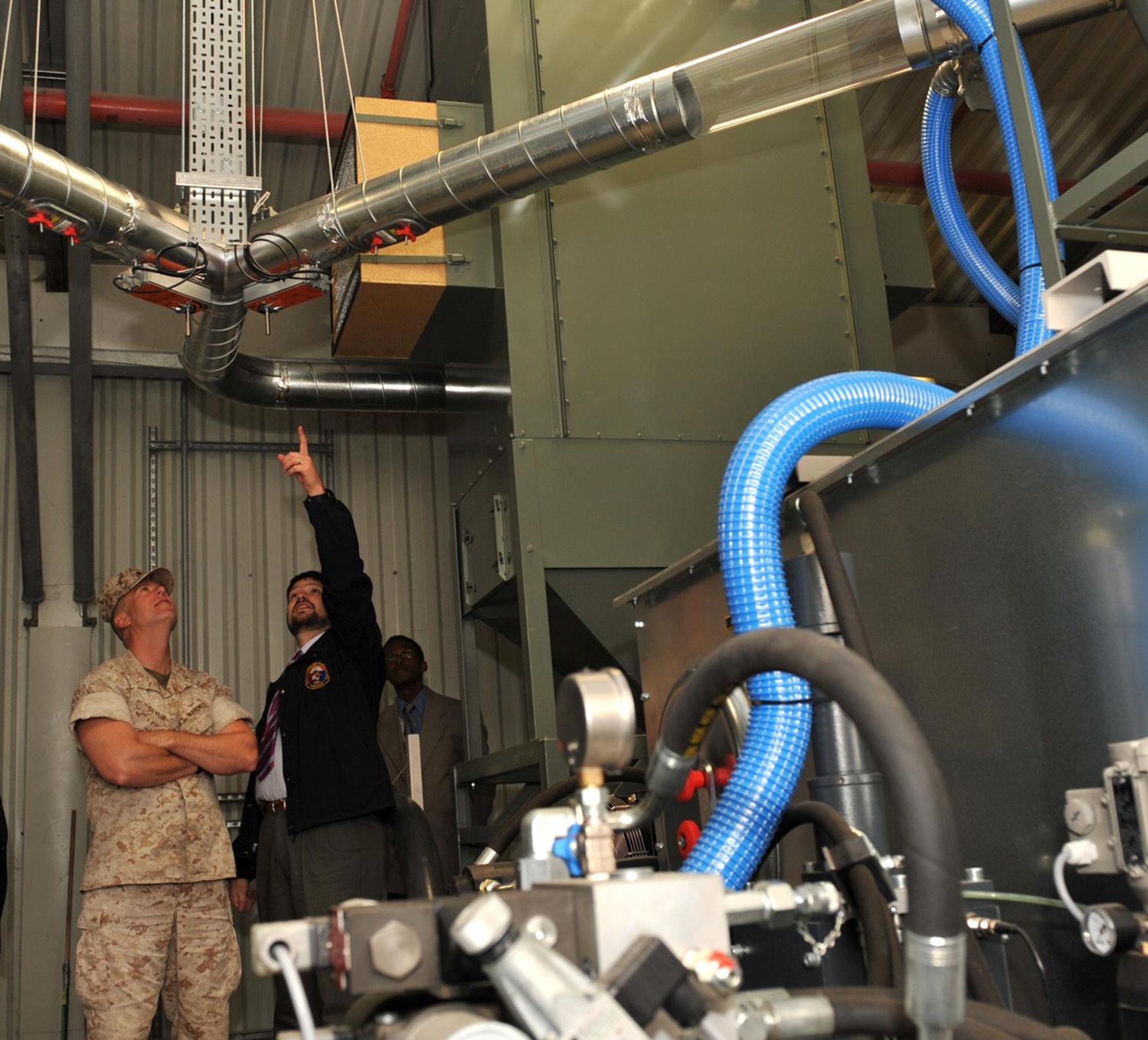 Mr. Joe Bowen, Chief of the JAC Security Support Office points out to JAC Commander, Marine Corps Colonel Pete Devlin the conduits that carry newly disintegrated paper waste from the shredder to the machine that compacts the material into puck like briquettes. Col Devlin tossed the first burn bag into the new machine at RAF Molesworth on April 26th. U.S. Air Force Photo by Staff Sgt. Javier Cruz. 