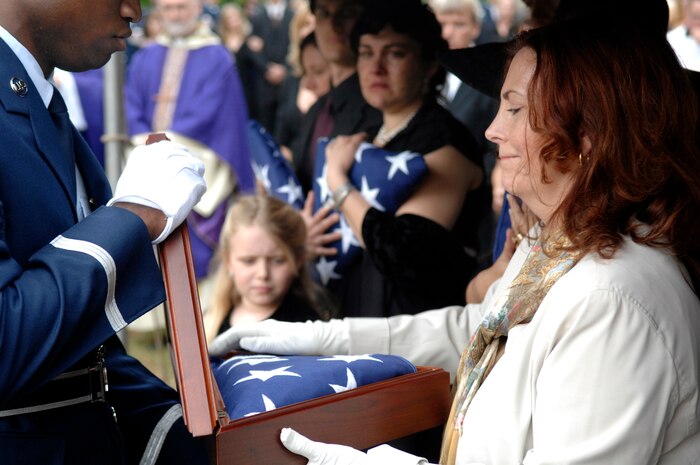 Staff Sgt. Akeem Parks helps Carmen Mikolajcik retire the American flag as three generations of Mikolajciks observe the rendering of honors after the funeral ceremony April 24, 2010, at the Cathedral of St. John the Baptist in Charleston, S.C. Sergeant Parks is an honor guard member from the 628th Logistics Readiness Squadron and Mrs. Mikolajcik is the widow of retired U.S. Air Force Brig. Gen. Thomas R. Mikolajcik. (U.S. Air Force photo/Senior Airman Timothy Taylor)