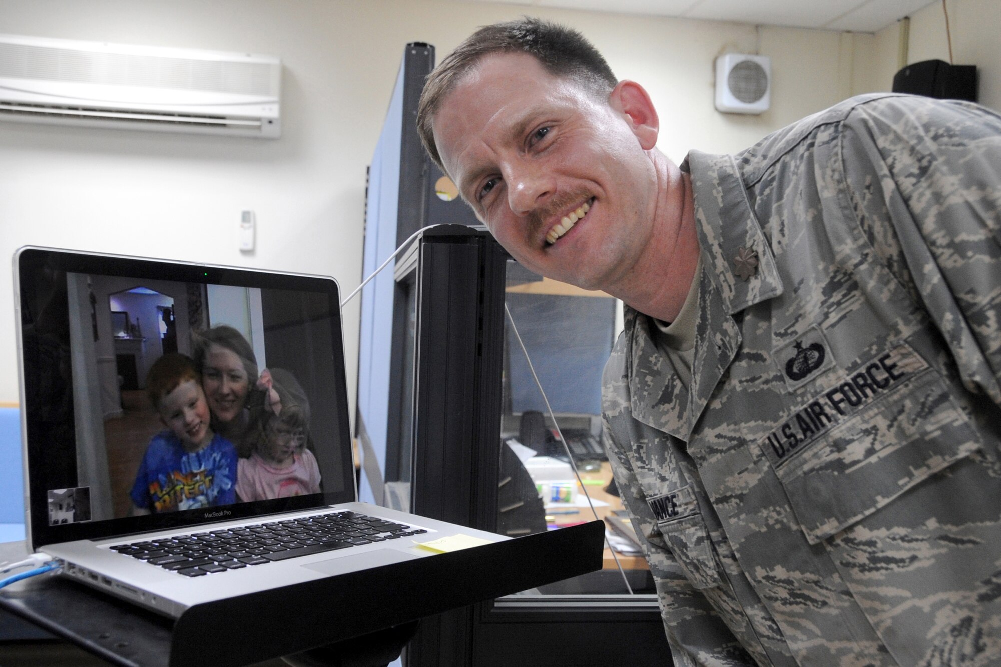 Maj. Brian Vance, finance chief, 380th Air Expeditionary Wing at an undisclosed base in Southwest Asia, poses for a family portrait via a laptop computer screen while connected to his wife and four-year-old twins who were in Virgina. Major Vance utilized the Voice over Internet Protocol or VoIP service offered at the Seven Sands Chapel so his family could observe his promotion ceremony while he was deployed which was about to take place March 31, 2010. (U.S. Air Force Photo/Senior Airman Jenifer H. Calhoun/Released)