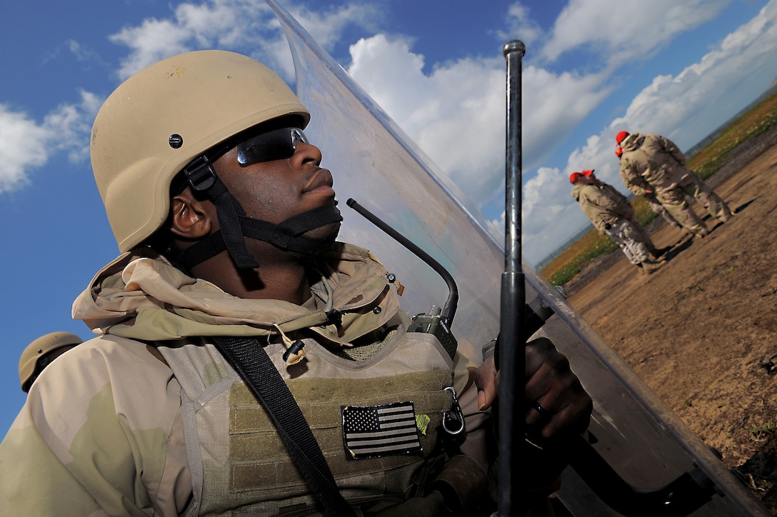 U.S. Navy Petty Officer 3rd Class Jason Henry takes cover behind a riot shield as training observers, in background, meet at a simulated forward operating base during a Navy Expeditionary Combat Command exercise in San Diego, April 21, 2010. Henry is assigned to Maritime Expeditionary Security Squadron 3.