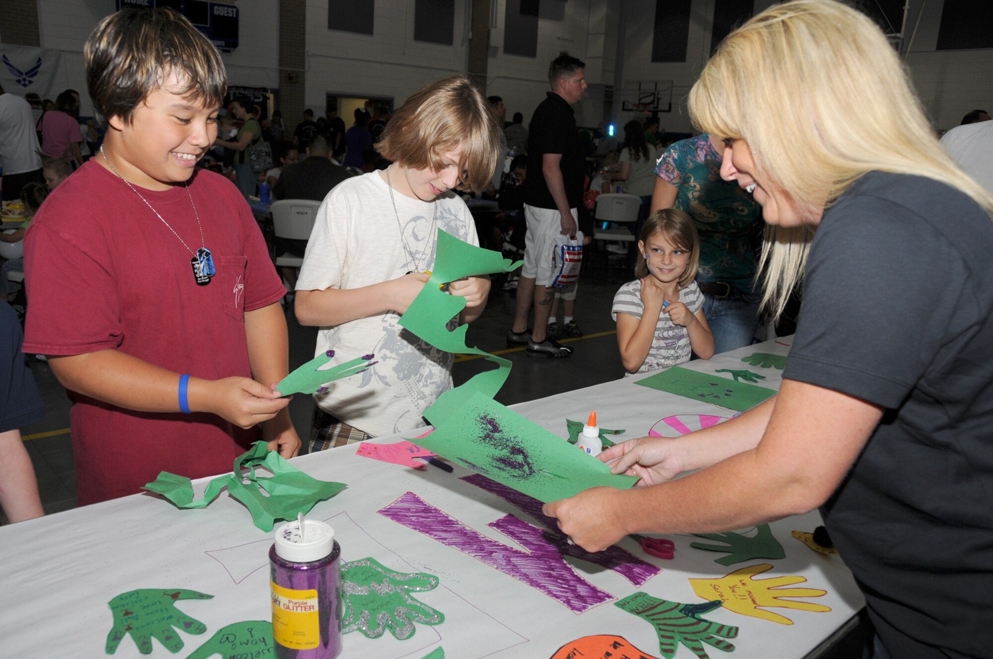 From left, Andrew Lutz, 11, and his friend Nathan Broom, 10, decorated their hand-shaped cutouts for a welcome home banner for deployed Airmen being prepared by Master Sgt. Jessica Woodruff, airman and family readiness center during Child Pride Day, April 24 at the youth center.  Andrew's parents are Oksun and retired master sergeant Ed Lutz, and Nathan's parents are Nathan and Tamra Broom.  (U.S. Air Force photo by Kemberly Groue)