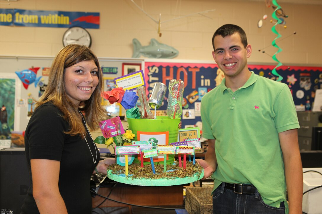 Hailee-Ann Hussey (left) and Jason Hall Jr. (right), biology classmates at Lejeune High school aboard Marine Corps Base Camp Lejeune, show off their recycling model during a class presentation, April 30.  Hussey and Hall collected more than 100 pounds of aluminum, which they took to Swansboro Recycling Center and used the profits to improve flowerbeds outside of Lejeune High School.