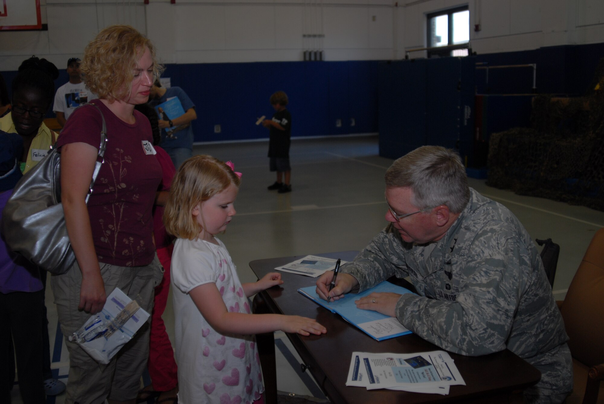 Maj. Gen. Kurt Cichowski, Air Force Special Operations Command vice commander, signs a copy of the book "Mercedes and the Chocolate Pilot" for Olivia Hooten as her mother Jill looks on during the Military Child Education Coalition's "Tell Me a Story" program hosted by the Airman & Family Readiness Center's School Liaison Program at Hurlburt Field, April 25. The book reading was scheduled as part of the base's events for the Month of the Military Child. (DoD photo by U. S. Air Force Staff Sgt. Orly N. Tyrell/Released)