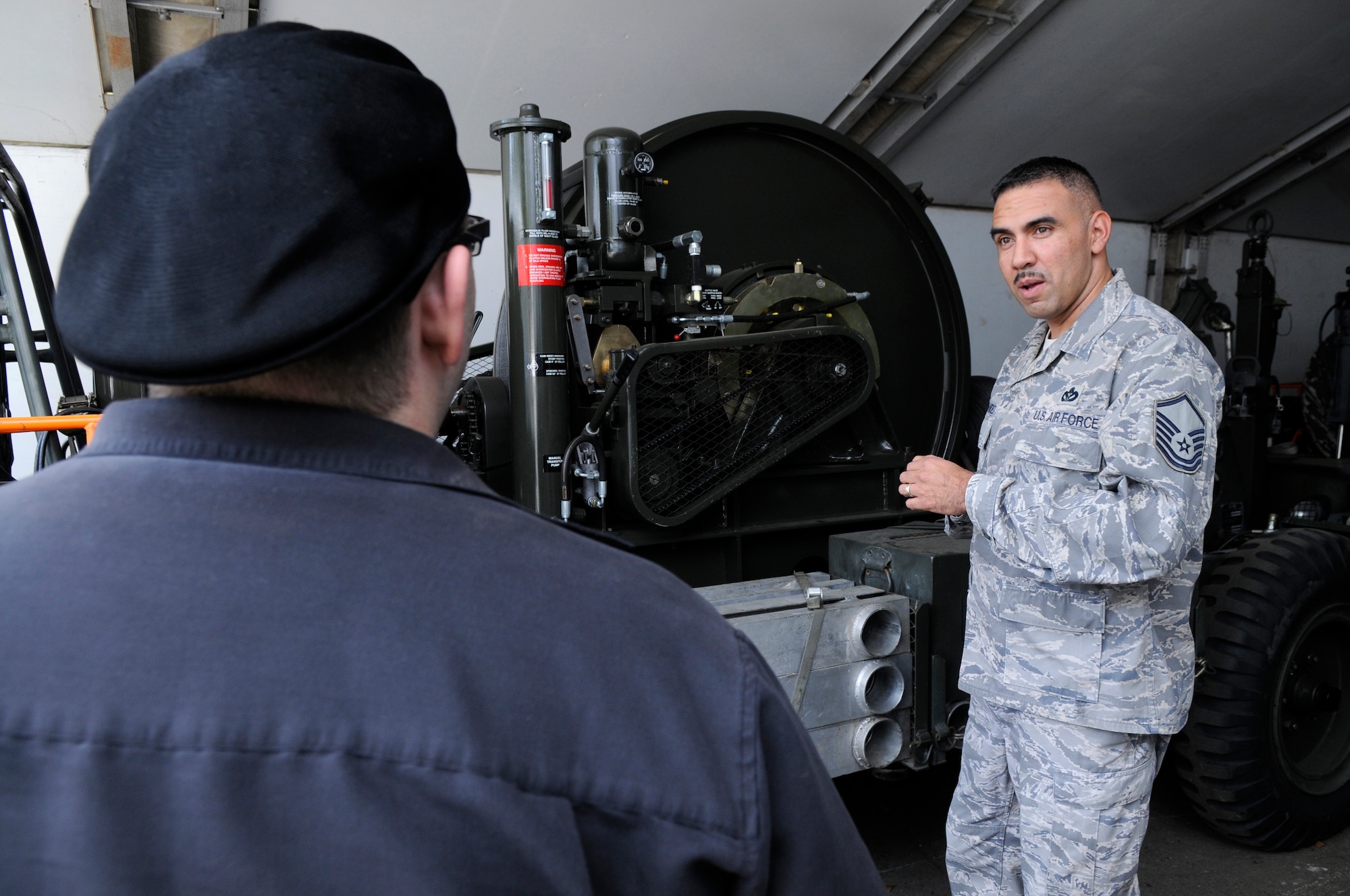 Mason Mastroianni, artist of B.C. comic strip, receives information on a Mobile Aircraft Arresting System from U.S. Air Force Master Sgt. Francisco Hernandez, 435th Contruction Training Squadron, superintendent, command aircraft arresting system depot operations, Ramstein Air Base, Germany, April 29, 2010. Mr. Mastronianni is one of 9 professional cartoonist from the National Cartoonist Society that visited various areas on Ramstein as part of a morale tour in cooperation with the United Service Organizations. (U.S. Air Force photo by Airman 1st Class Brittany Perry)