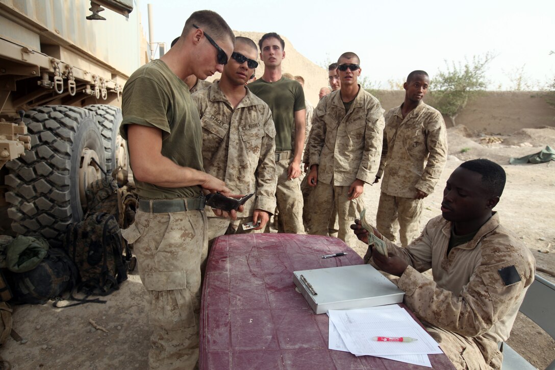 Cpl. Kofi Agyeman, 24, from Wilmington, Del., a Ghanaian native, disburser with Headquarters and Service Company, 1st Marine Logistics Group (Forward), disburses casual pay to a few Marines during a Warrior Express Services Team mission in northern Helmand Province, July 16-30. A WES Team consists of a disburser and a mobile Post Exchange, or PX. They provide service members located at remote forward operating bases and combat outposts a chance to get some cash to buy a few things from the mobile PX.