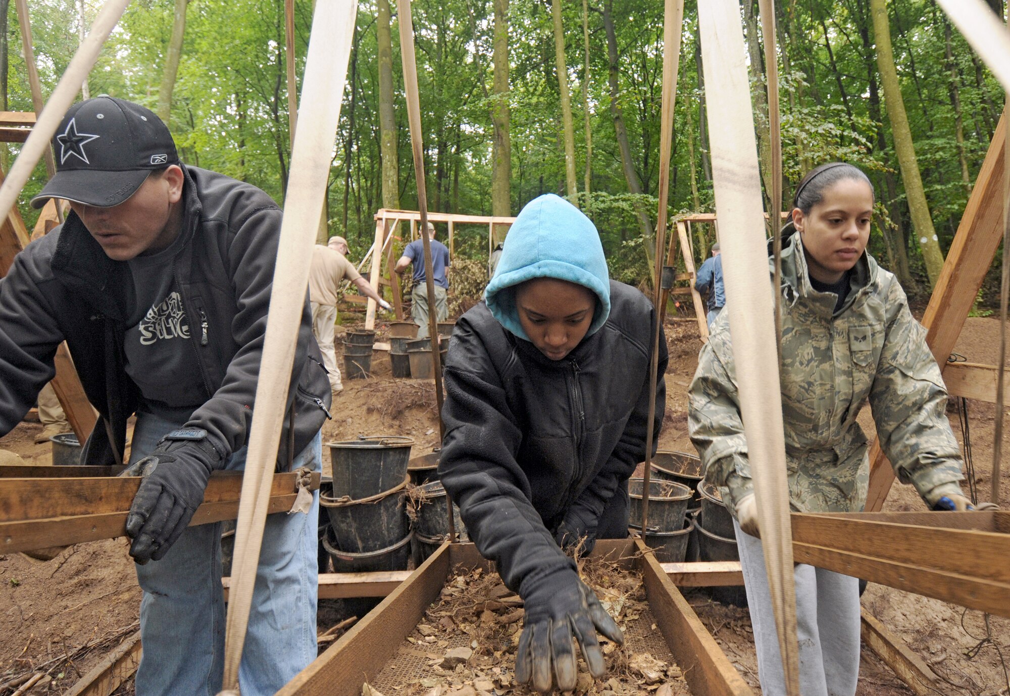 Master Sgt. Austin Lewis (left to right), Senior Airman Candice Anderson and Senior Airman Emmannuelle Canty sift through dirt while volunteering for a Joint Prisoners of War/Missing in Action Accounting Command mission July 28, 2010, in Rheinland-Pfalz, Germany. Volunteers from the Spangdahlem community assisted JPAC on their mission to recover wreckage from an aircraft that crashed on a local logging trail during World War II. Sergeant Lewis is assigned to the 726th Air Mobility Squadron. Airmen Anderson and Canty are from the 52nd Force Support Squadron. (U.S. Air Force photo/Staff Sgt. Benjamin Wilson)
