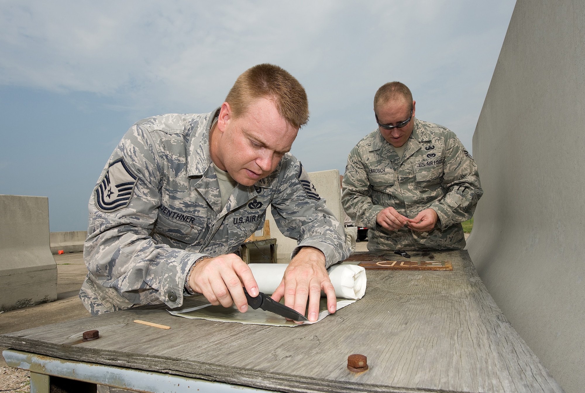 Master Sgt. David Guenthner, (left), 512th Civil Engineer Squadron Explosive Ordnance Disposal Flight program manager here, cuts out a piece of deta sheet, while Senior Airman John Larosch, a 512th EOD technician, places portions of deta sheet on to a steel plate at the EOD demolition range here, July 29. The technicians were testing a theory to see how much deta sheet it took to penetrate steel after detonation. (U.S. Air Force photo/Jason Minto) 
