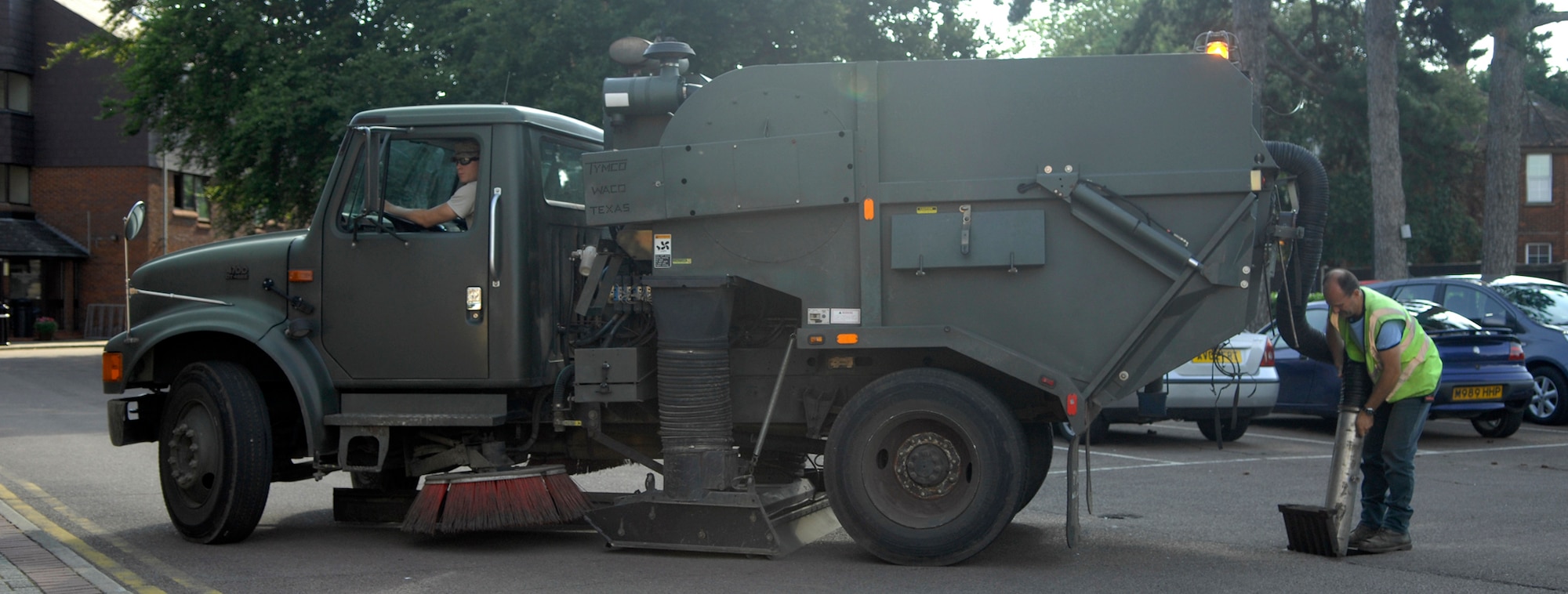 RAF MILDENHALL, England -- Richard "Spot" Austin, 100th Civil Engineer Squadron, vacuums leaves and other debris from a water drain in a parking lot here Aug. 3, while Senior Airman Jordan Lamm runs pumps from the cab of their truck.  The yearly task takes several months to complete and covers thousands of drains.  (U.S. Air Force photo/Staff Sgt. Austin M. May)