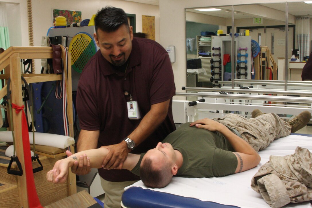 Physical Therapy Technician Frank Gonzales stretches out the arm of Cpl. Justin Reeves, a Marine with 3rd Light Armored Reconnaissance Battalion during physical therapy Wednesday at the Robert E. Bush Naval Hospital. Reeves, who's dislocated his shoulder multiple times, is now recovering after surgery.