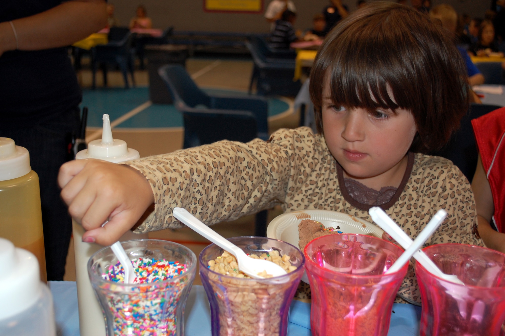 Little Warrior Haleigh, 5, grabs a spoonful of multicolored sprinkles for her bowl of ice cream during Brainfreeze July 22. A variety of toppings were provided to include peanuts, cookies, cherries, M&M’s, crushed candies and an assortment of syrups. (U.S. Air Force photo/Airman 1st Class Kristina Overton)