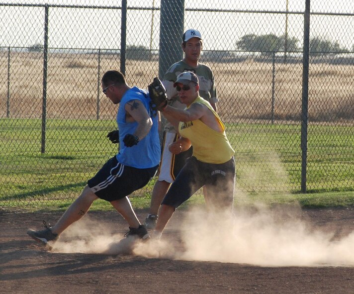 Airman 1st Class James Lowe, 9th Intelligence Squadron, stops safely in front of a tage at third base by 2nd Lt. Thomas Uhl, 9th Security Forces Squadron as Mr. Dan Helton looks on, Aug 2 during an intramural softball game. The 9th IS led the entrie game, winning 17-9. (Photo by Senior Airman Chuck Broadway)
