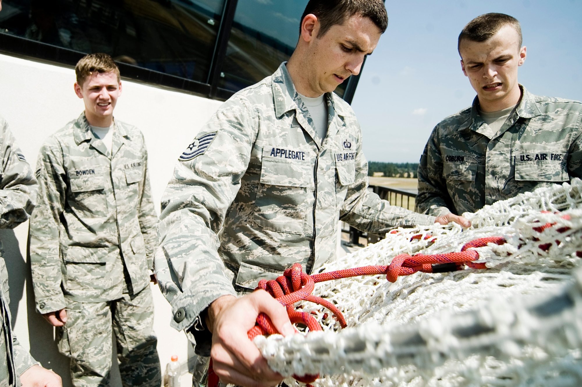 Airman 1st Class Manuel Bowden, left, and A1C Andrew Coburn look on as Tech. Sgt. Jordan Applegate stows the Baker Life Chute after completing a bi-annual familiarization training exercise Aug. 3. (U.S. Air Force Photo/Abner Guzman)