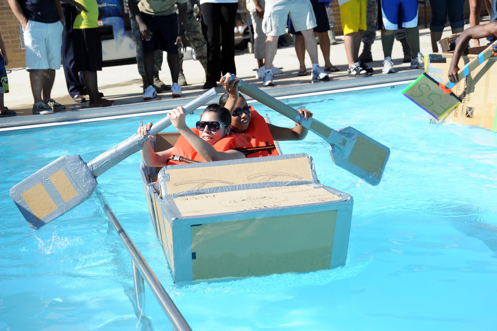 Senior Airman Tairesa Holland and Airman 1st Class Stephanie Martinez compete during the cardboard regatta race at the Warhawk Pool July 30. The race was part of the "Sizzling Summer Block Party" sponsored by the 802nd Force Support Squadron. The party included a disc jockey, children's activities, indoor sports activities, a dunking booth and an outdoor movie at dusk. Airman Holland is with the 802nd Logistics Readiness Squadron; Airman Martinez is with the 802nd FSS.  (U.S. Air Force photo/Alan Boedeker)