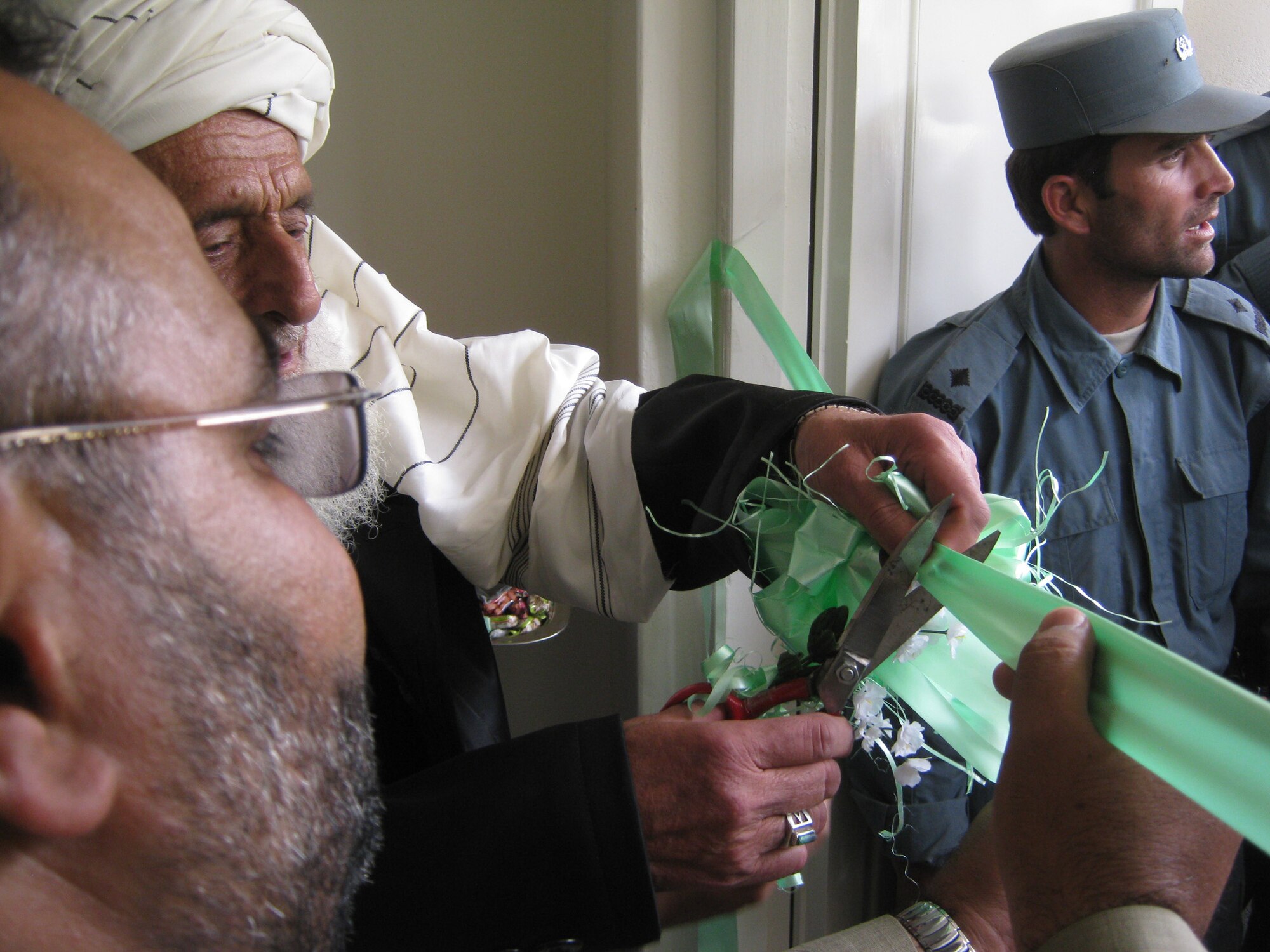 Panjshir Deputy Gov. Abdul Rahman Kabiri (front, left) holds a ribbon while a local judge cuts it to signify the opening of the Paryan Justice Center in the Panjshir Province, Afghanistan. In addition to Kabiri, senators, various district governors, Provincial Reconstruction Team Panjshir members and Afghan journalists were in attendance to witness the ceremony. (Photo by U.S. Air Force 2nd Lt. Jason Smith, PRT Panjshir Public Affairs)