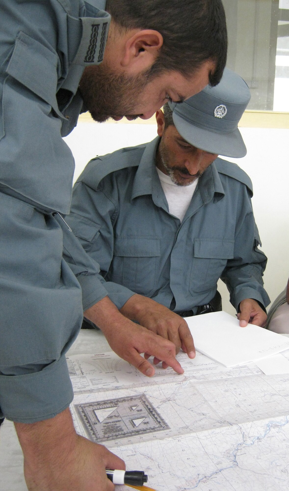Afghan National Police Capt. Safat Ullah Sangee, Panjshir Operations Coordination Center-Provincial, helps a Rokha District ANP member with map and compass reading techniques during a July 13 class. This class was the second day of Sangee?s three-day course at the Rokha Police Headquarters. Some of the things Sangee taught included how to use a protractor with a map, give grid coordinates, find grid coordinates, identify terrain features and measure distance between points. (Photo by U.S. Air Force 2nd Lt. Jason Smith, PRT Panjshir Public Affairs)