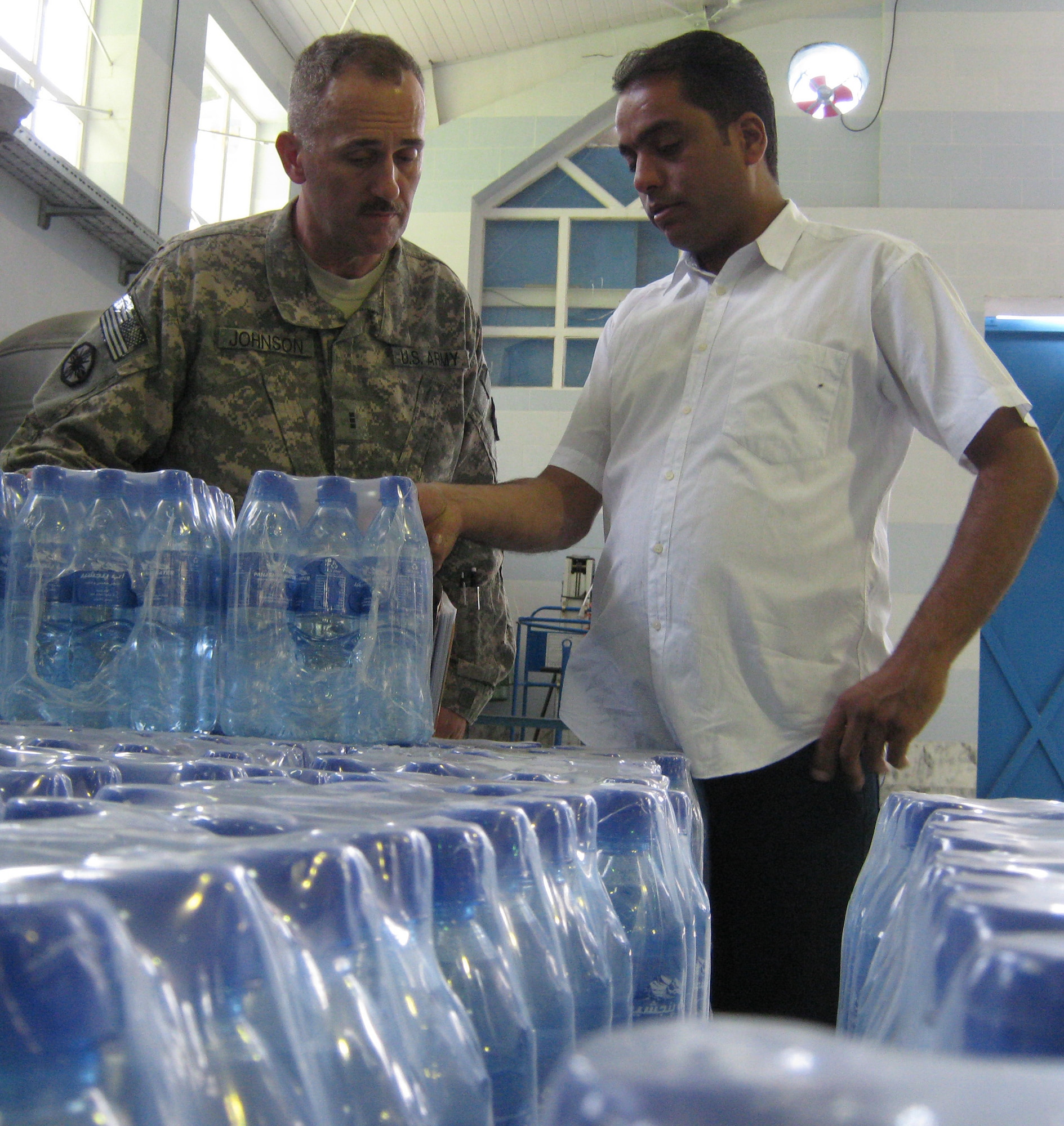 Ali Rezayi, Panjshir Beverage Industry LTD quality control manager, shows Army Chief Warrant Officer Peter Johnson, 72nd Medical Detachment Veterinary Services, some of the final product the water bottling plant produces. Johnson spent July 11 pre-auditing the water bottling plant in the Khenj District of the Panjshir Valley, Afghanistan. (Photo by U.S. Air Force 2nd Lt. Jason Smith, PRT Panjshir Public Affairs)